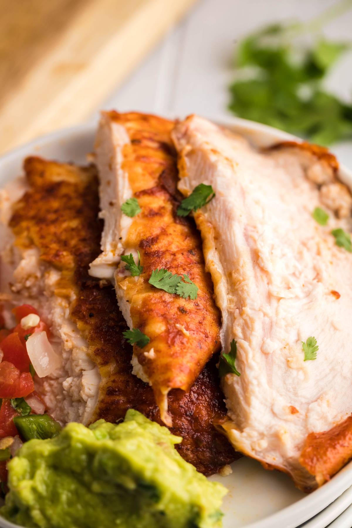 Sliced Traeger Beer Can Chicken breast with fresh cilantro, guacamole, and diced tomatoes on a white plate.