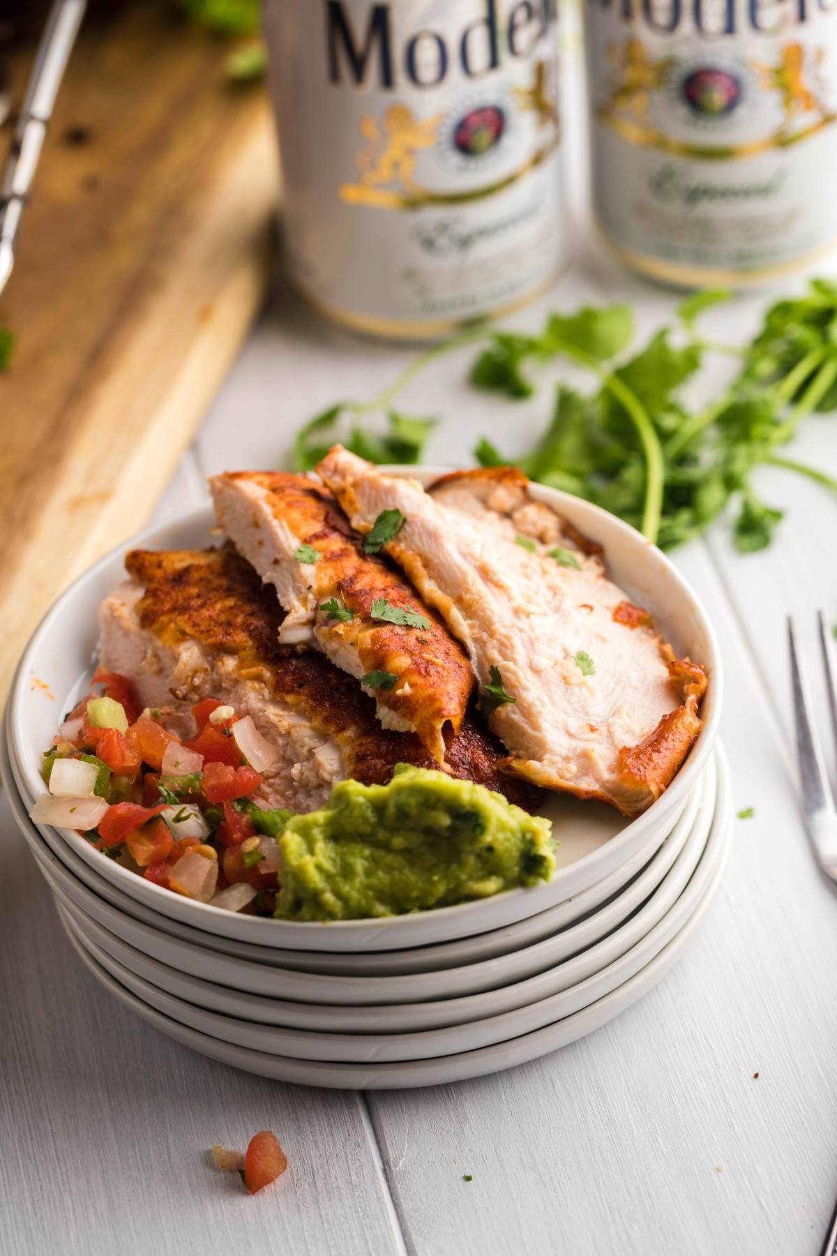 A plate with Traeger beer can chicken, pico de gallo, refried beans, and guacamole, with beer cans in the background.