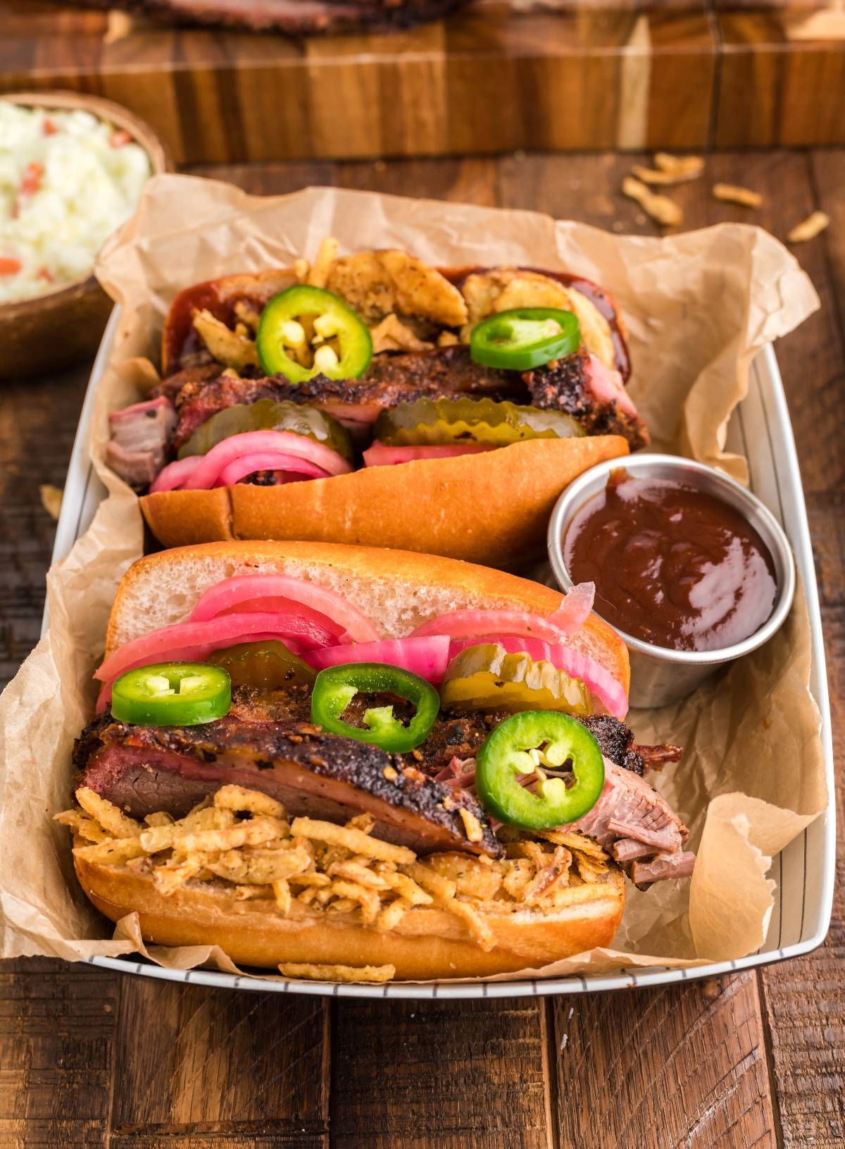 Enjoy the best BBQ brisket sandwich with classic brisket sandwich toppings—pickles, jalapeños, and onions—all served with barbecue sauce in a tray. Perfect for anyone craving a delicious sandwich using leftover brisket!.