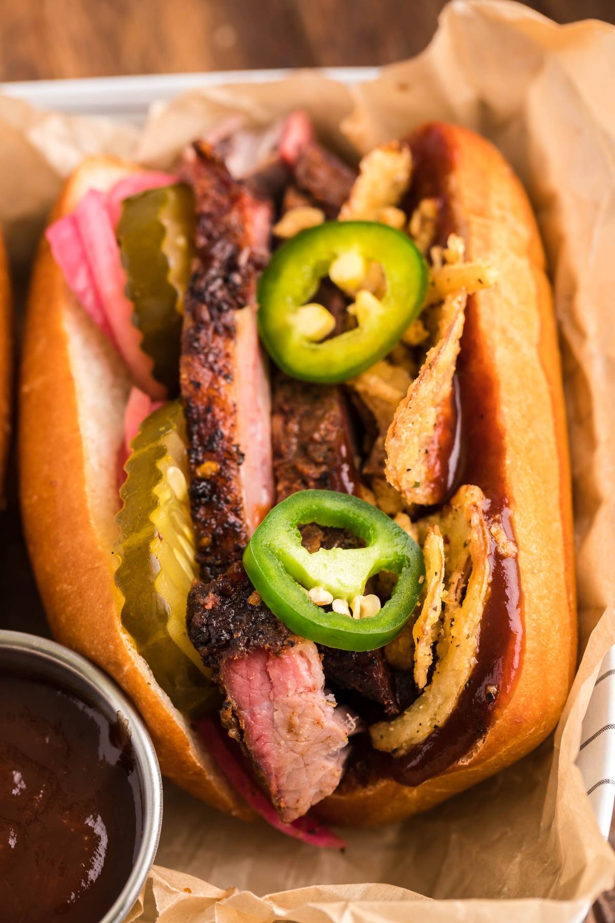 Smoked Brisket Sandwich piled high with sliced brisket, classic brisket sandwich toppings like pickles, crispy onions, jalapeño slices, and tangy sauce on a fresh bun—a perfect way to enjoy a sandwich using leftover brisket.