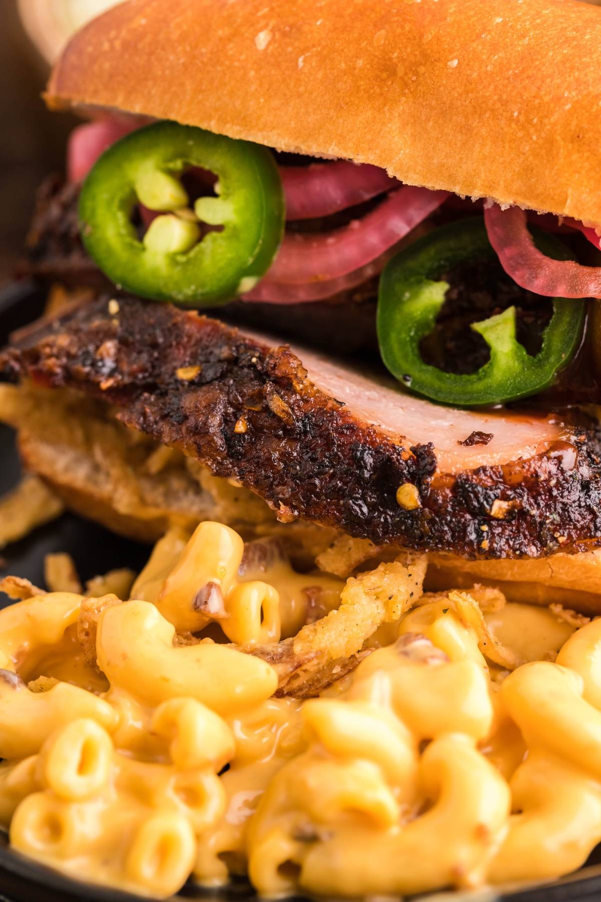Close-up of the best BBQ brisket sandwich, stacked with homemade pickled red onions and jalapeños, served alongside creamy macaroni and cheese.