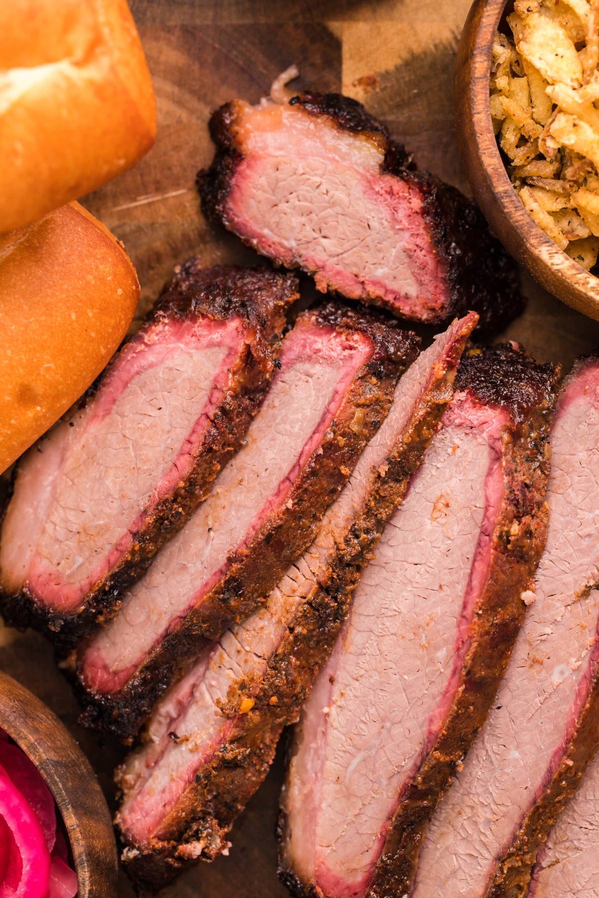 Sliced smoked brisket with a dark bark and pink smoke ring, served on bread with classic brisket sandwich toppings like pickled onions—a perfect Best BBQ brisket sandwich or a great sandwich using leftover brisket.