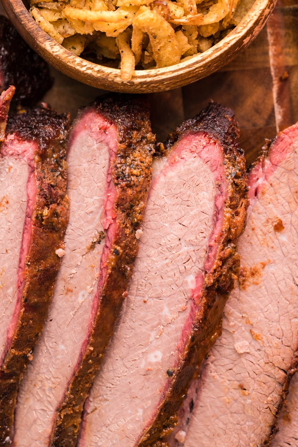 Sliced smoked brisket with a dark crust, next to a bowl of crispy fried onions—perfect for creating the Best BBQ brisket sandwich.