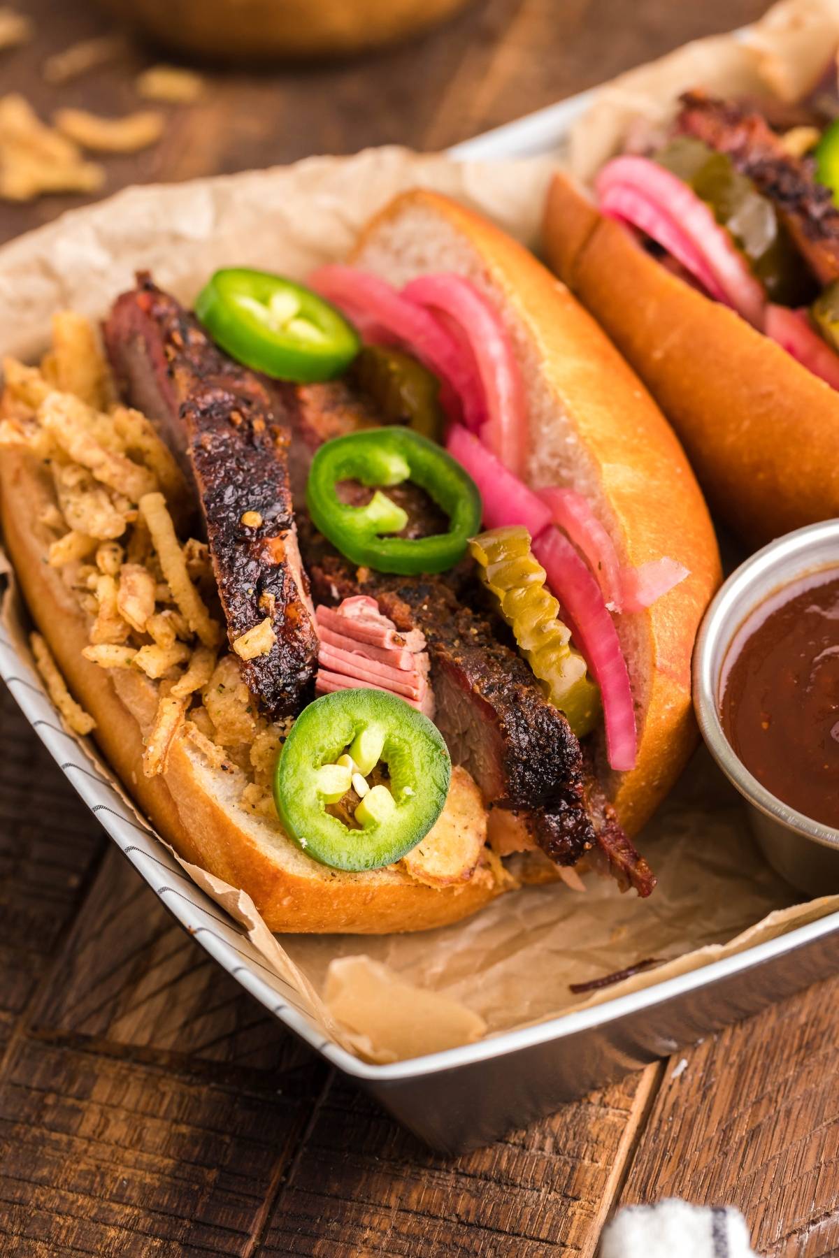 Brisket sandwich using leftover brisket, topped with fried onions, pickles, jalapeños, homemade pickled red onions, and barbecue sauce served in a tray.