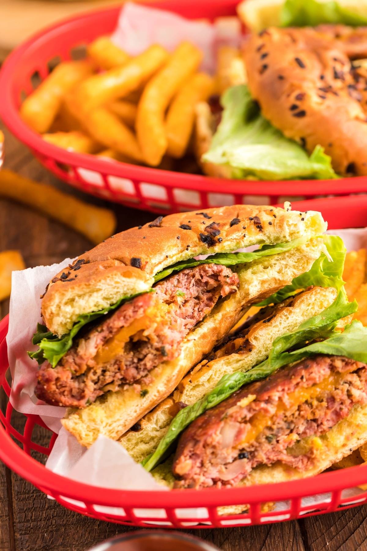 Close-up of a Smoked Cheddar Bacon Stuffed Burger with lettuce in a red basket, with fries in the background.