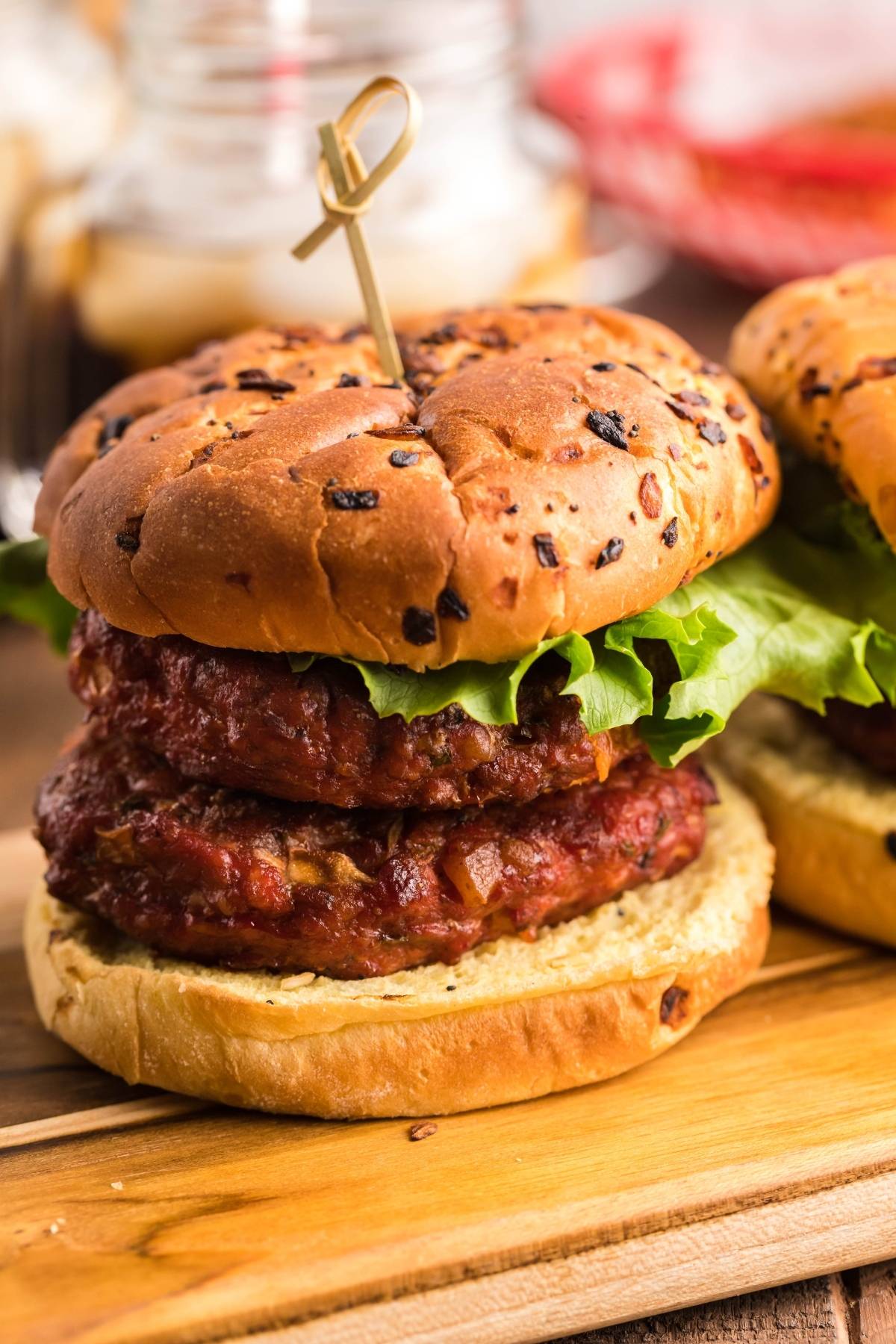 A double beef burger with lettuce served on an onion bun, featuring our signature smoked stuffed burger style, secured with a toothpick and presented on a wooden board.