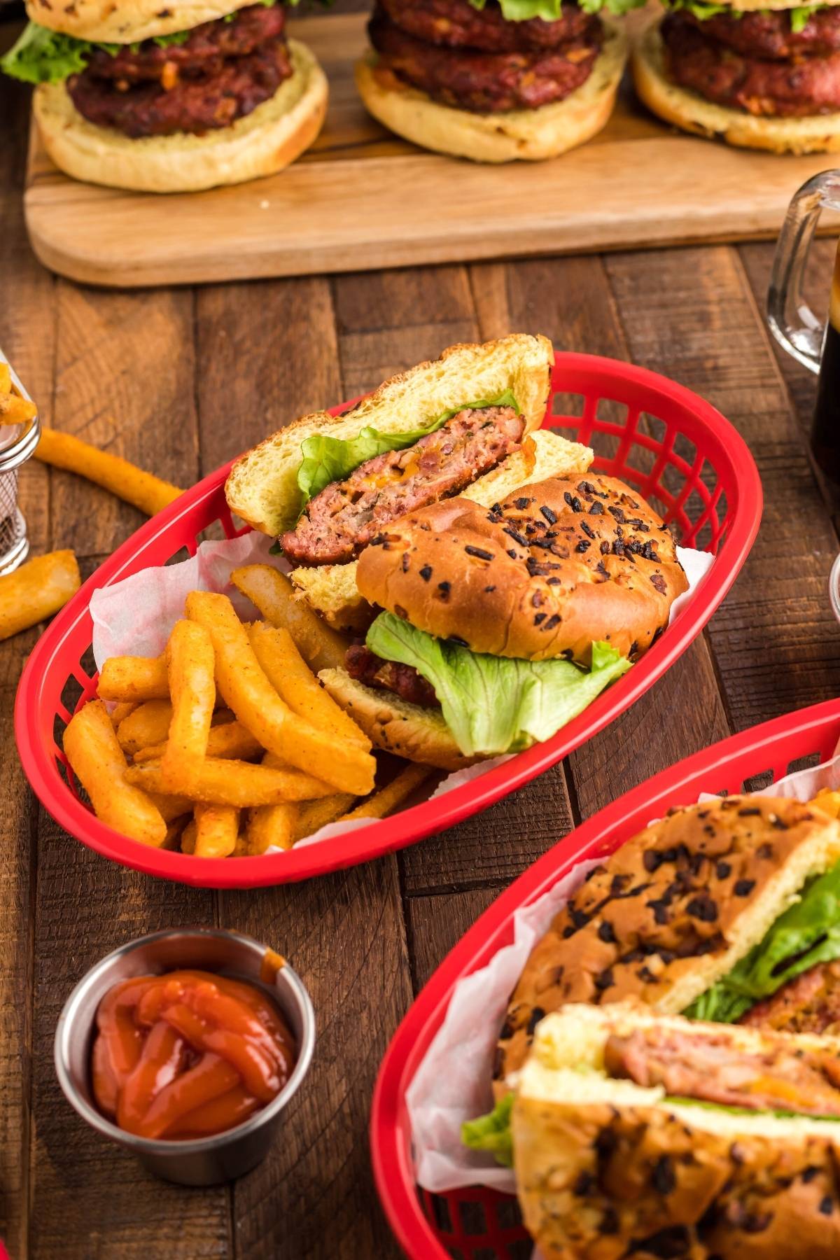 Burger with lettuce, onion bun, and crinkle fries in a red basket, featuring a Traeger grilled stuffed burger and ketchup on the side.