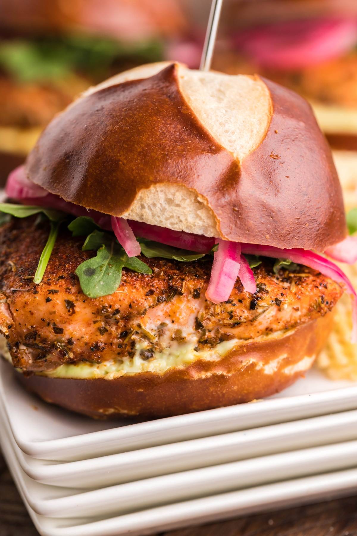 A smoked salmon slider with greens and pickled onions on a pretzel bun, served on a stack of white plates—perfect for trying your favorite smoked salmon recipe made in a pellet grill or Traeger.