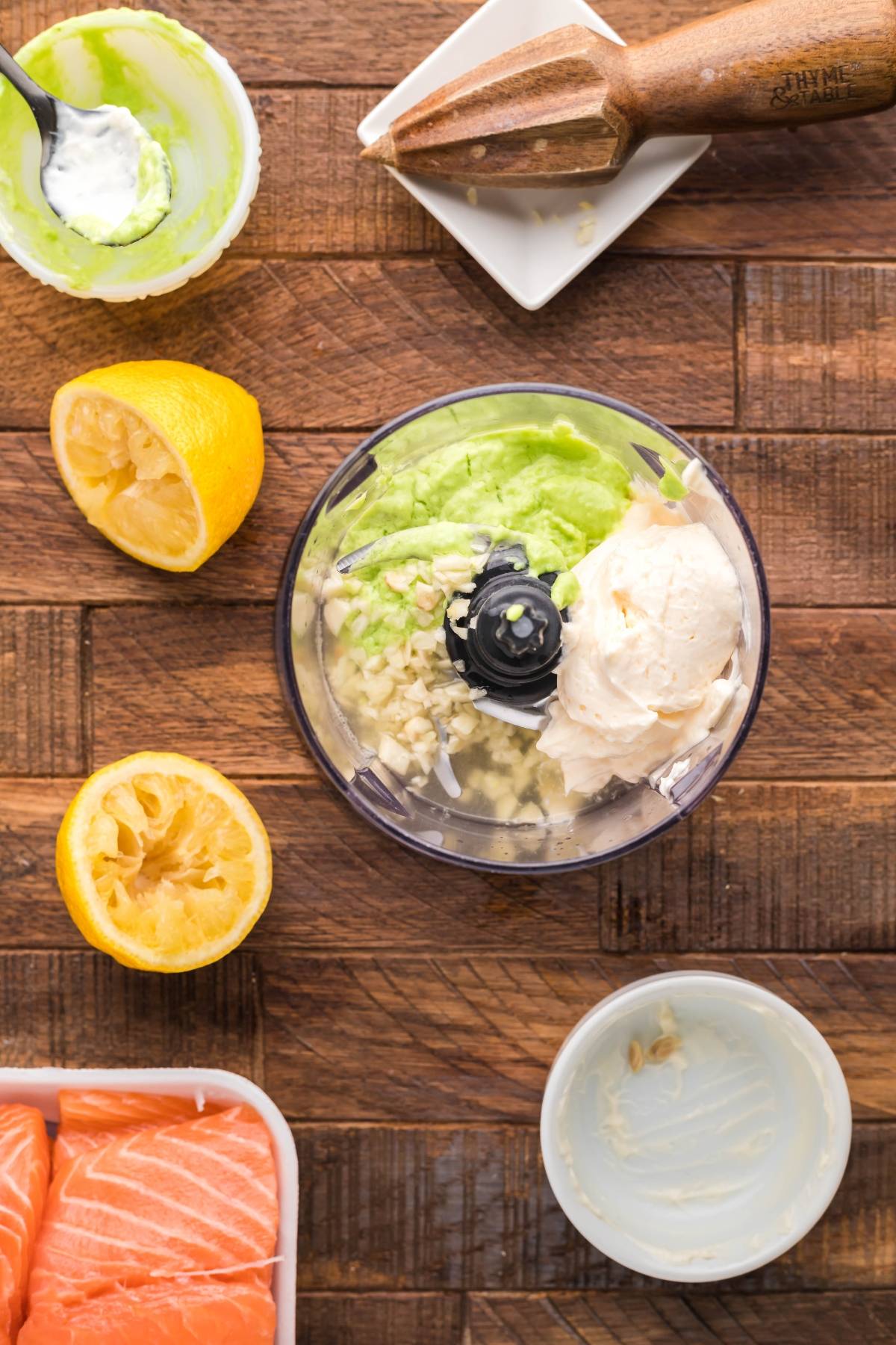 Mini food processor with avocado, cream cheese, and garlic, surrounded by lemon, juicer, and salmon—perfect for crafting Wasabi Mayo or a tasty smoked salmon recipe.