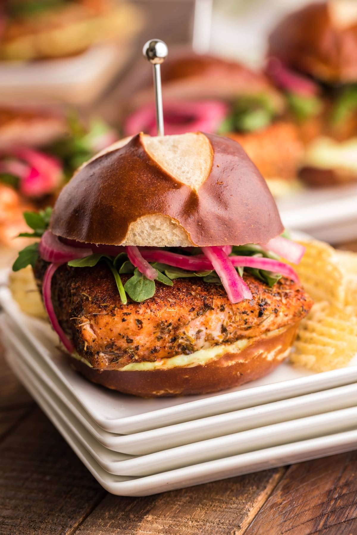 Smoked Salmon Sliders with onions and greens on a pretzel bun, served on stacked plates with potato chips—perfect for your next summer BBQ or as a must-try smoked salmon recipe.