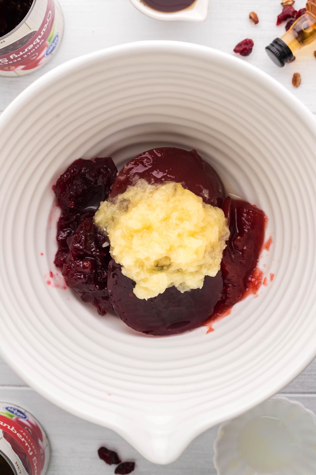 White bowl with cranberry sauce with bourbon and pineapple, surrounded by ingredients on a white surface.