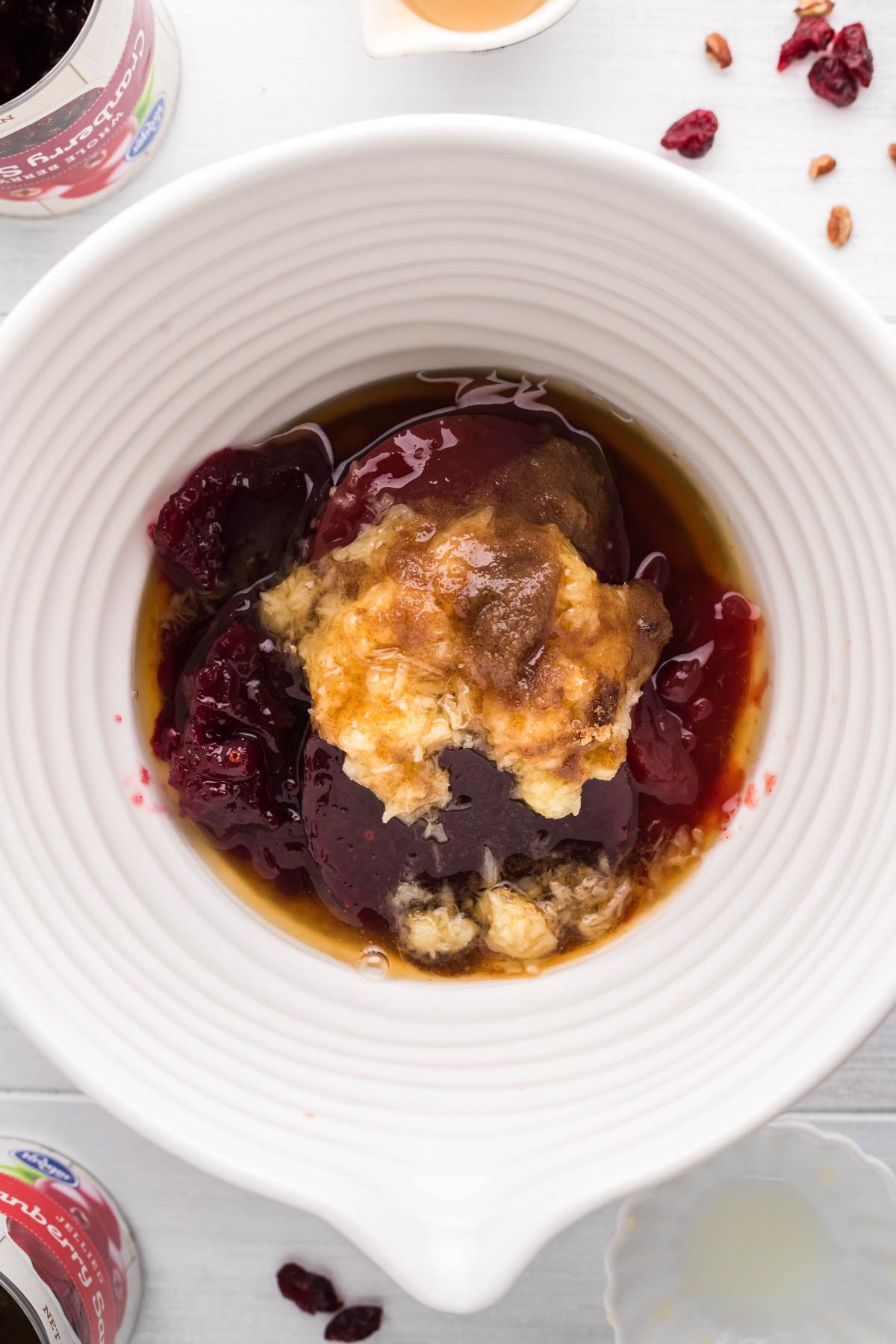 A white bowl with Spiked Cranberry Sauce, brown sugar, and syrup being mixed together on a white surface—perfect for trying a cranberry sauce with bourbon and pineapple.