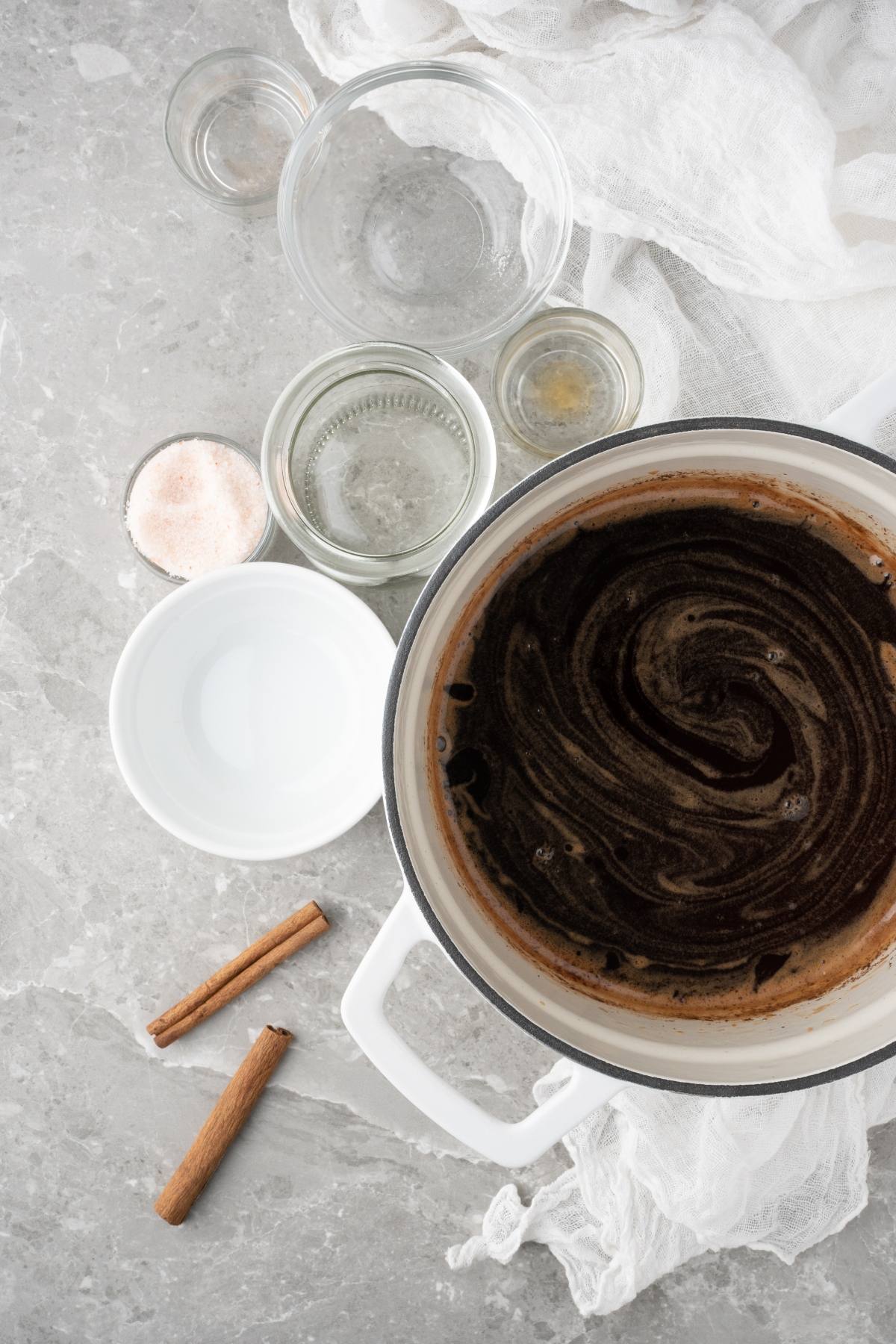 A pot of dark liquid with cinnamon sticks, salt, and small glass bowls on a gray countertop—perfect for crafting your own DIY cinnamon dolce latte or a Starbucks copycat latte at home.