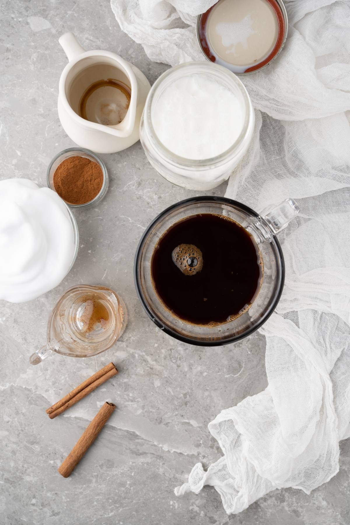 Top view of coffee, milk, foam, cinnamon sticks, cinnamon powder, and vanilla on a gray marble surface—perfect for crafting a Homemade cinnamon dolce syrup or your own Starbucks Cinnamon Dolce Latte.