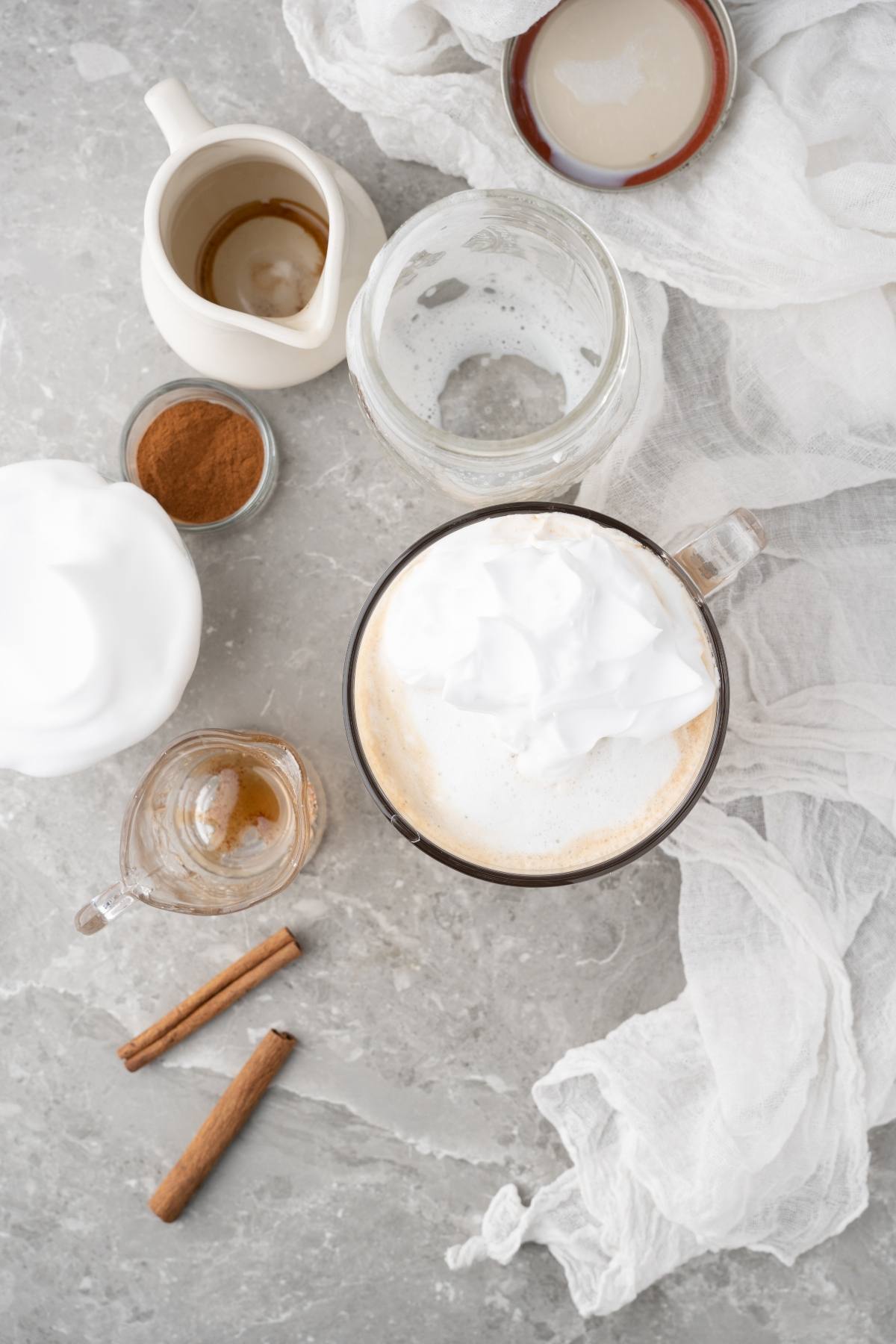 Enjoy a cozy DIY cinnamon dolce latte: coffee with whipped cream in a glass mug, cinnamon sticks, vanilla, and cream on a marble surface—a true Starbucks copycat latte experience at home.