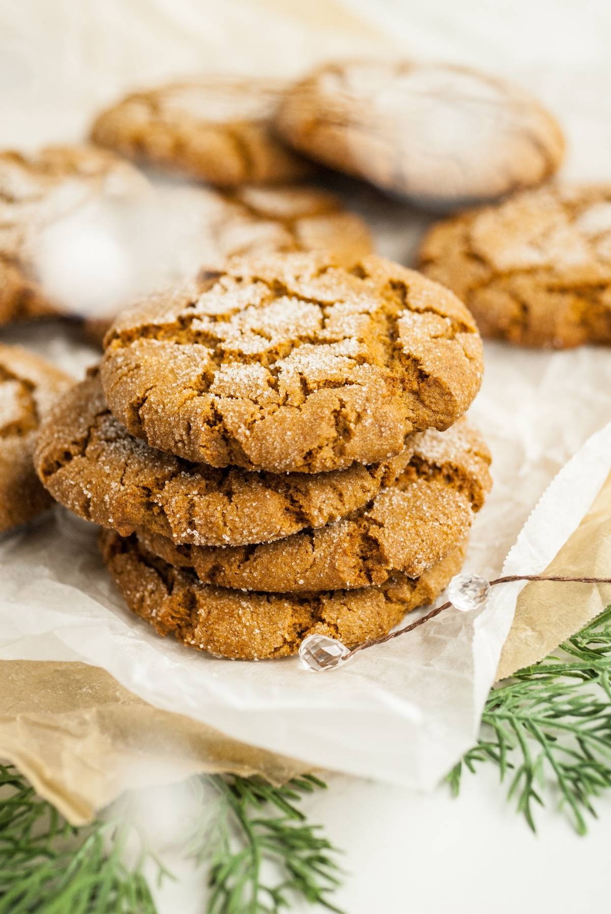 Three sugar-coated gingersnap molasses cookies stacked on parchment paper, with more cookies and greenery in the background.