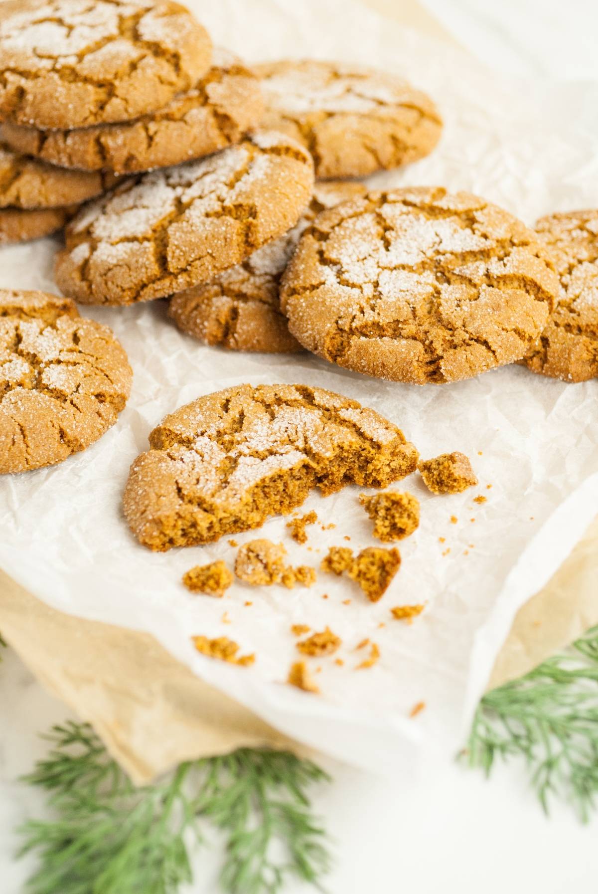A batch of sugar-coated ginger cookies, inspired by the best ginger molasses cookie recipe, sits on parchment paper—one with a bite taken out and crumbs scattered.