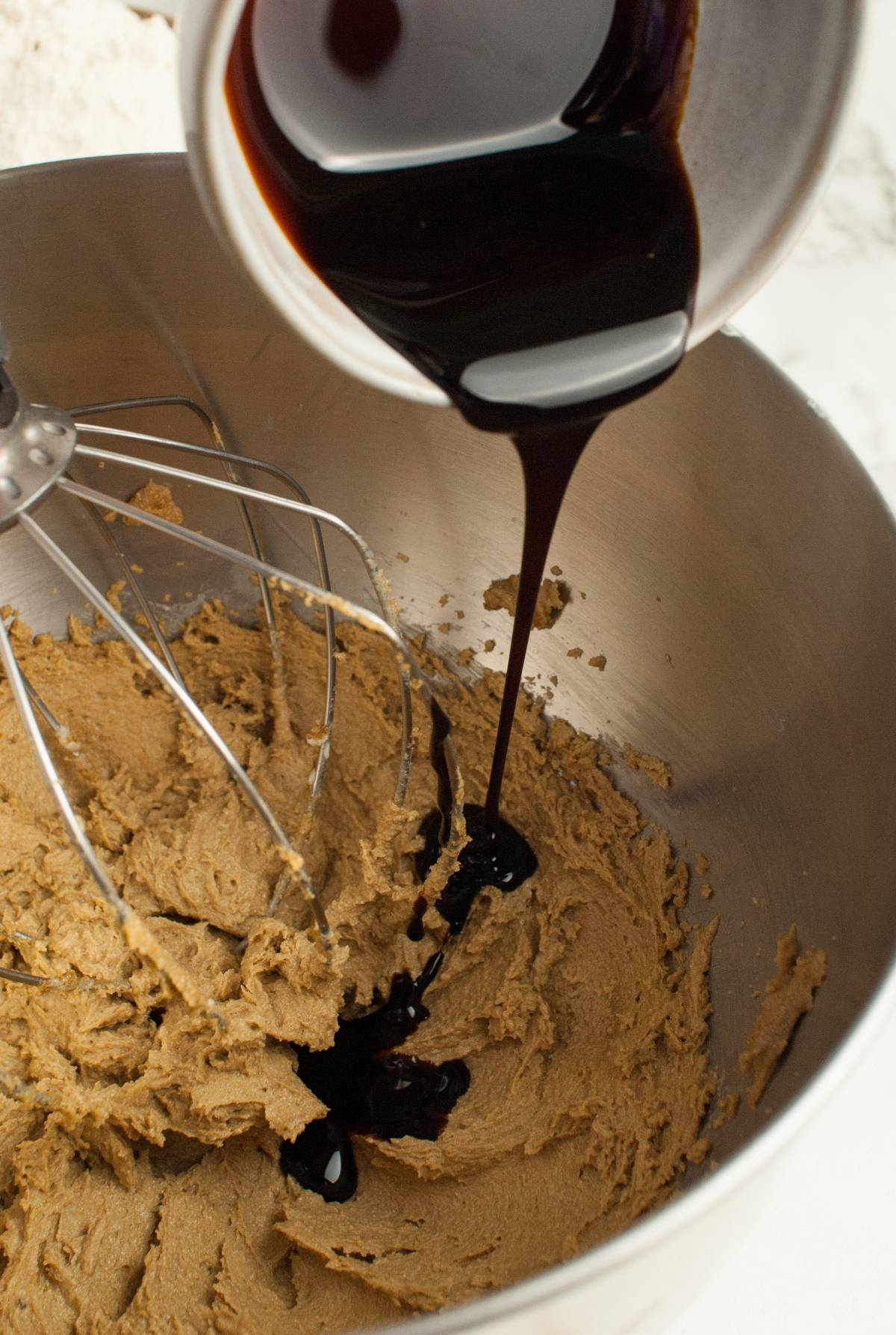 Dark liquid being poured into a mixing bowl with brown batter and a metal whisk, perfect for making homemade Starbucks gingerbread cookies.