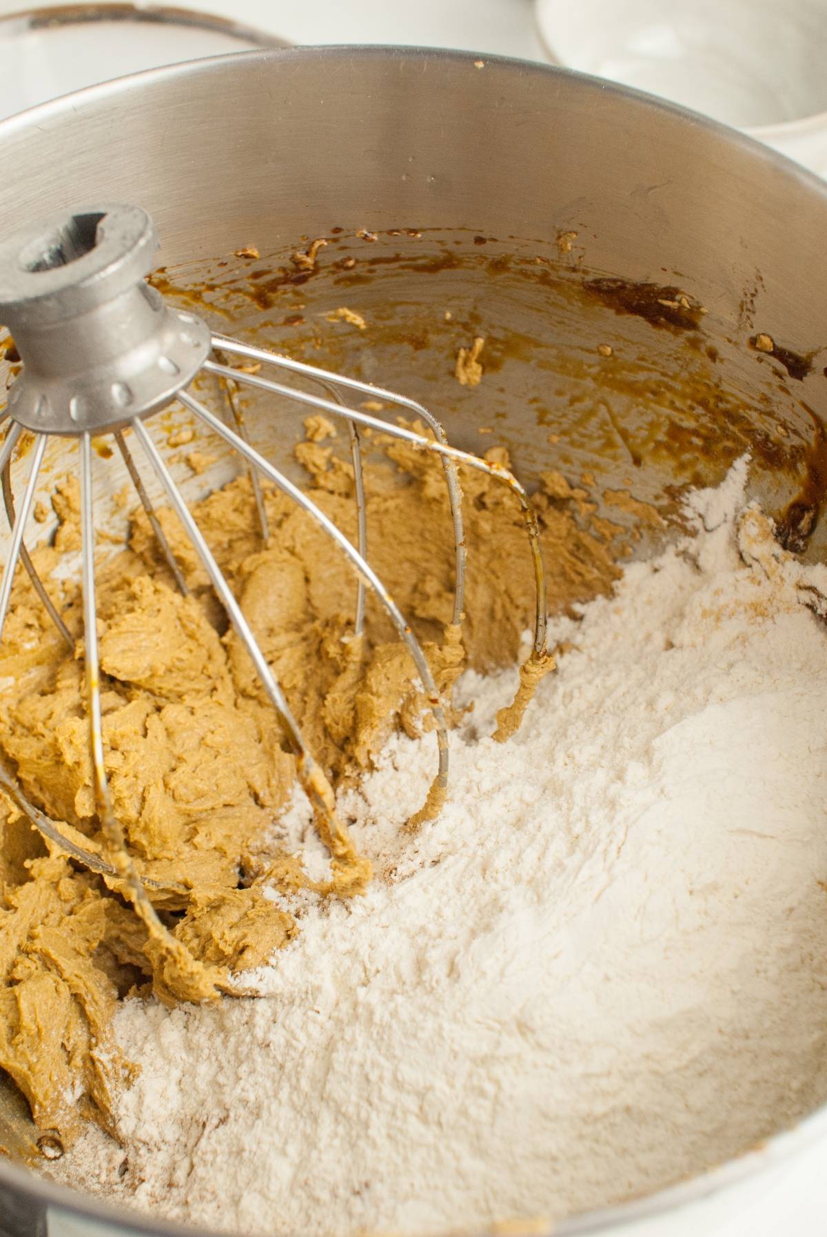 Close-up of cookie dough and flour being mixed in a stand mixer with a wire whisk attachment—perfect for creating the best ginger molasses cookie recipe or homemade Starbucks Christmas cookies.
