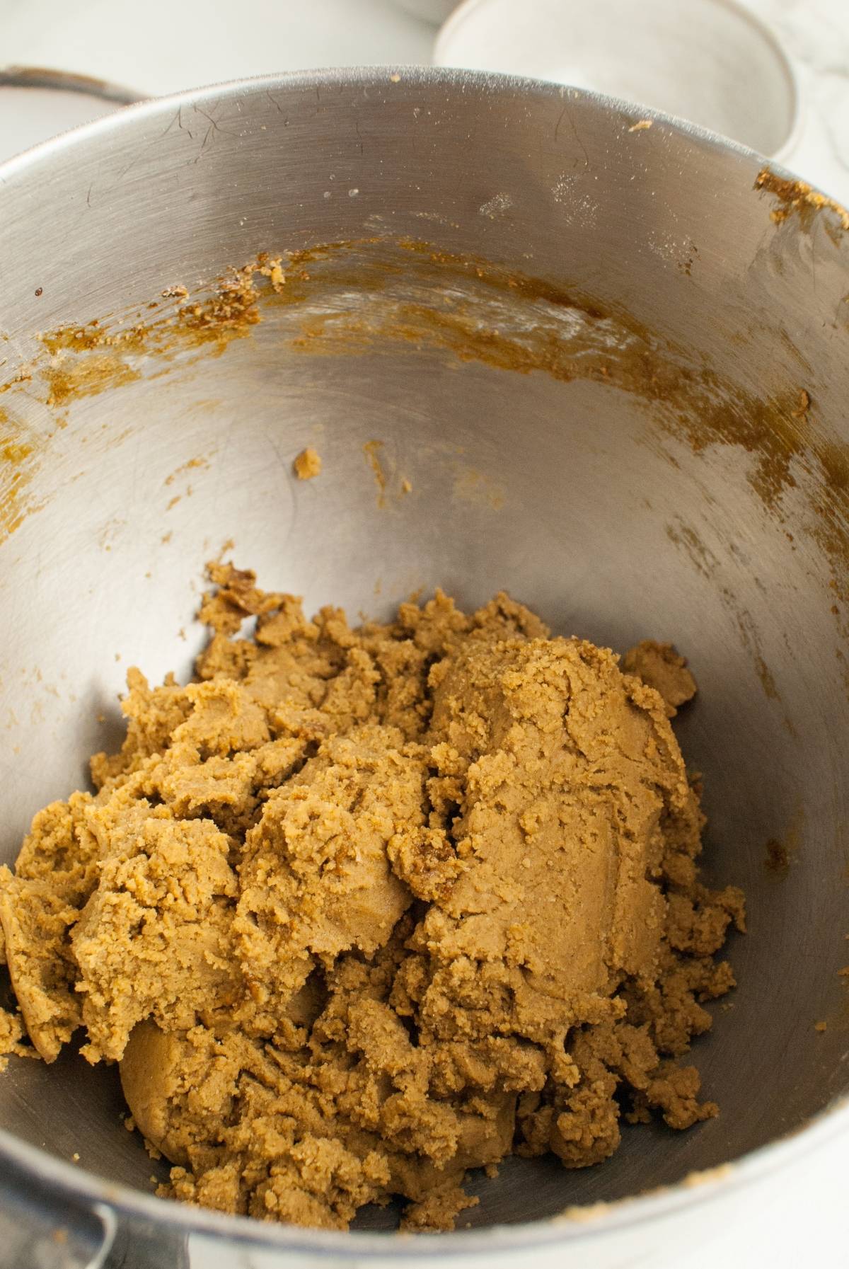 A metal mixing bowl containing brown cookie dough with some dough stuck to the sides, perfect for making the best ginger molasses cookie recipe inspired by Starbucks Copycat Ginger Molasses Cookies.