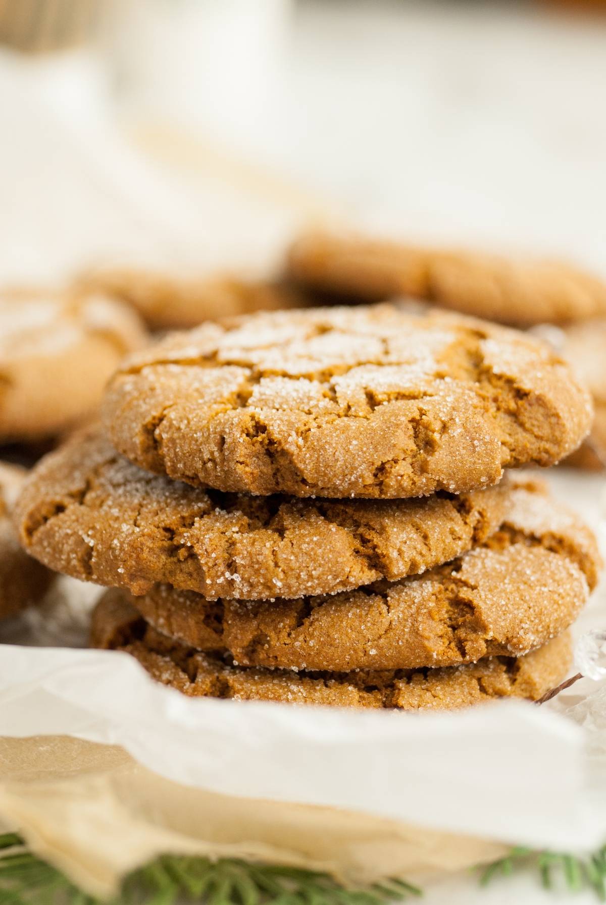 A stack of three sugar-coated gingersnap molasses cookies on parchment paper, with more homemade Starbucks Christmas cookies in the background.