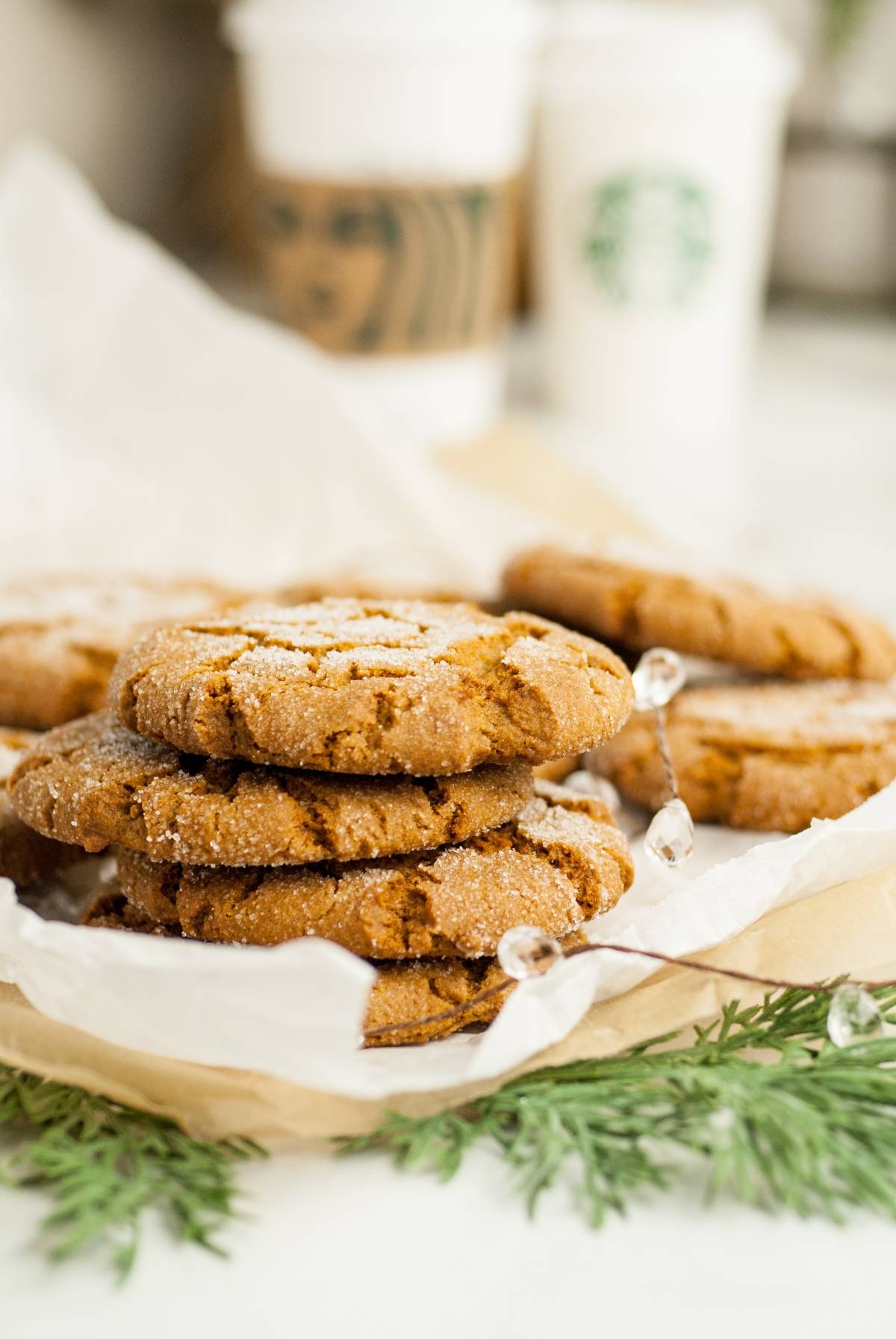 A stack of sugar-coated gingersnap molasses cookies on parchment paper with Starbucks cups in the background, capturing that homemade Starbucks Christmas cookies vibe.