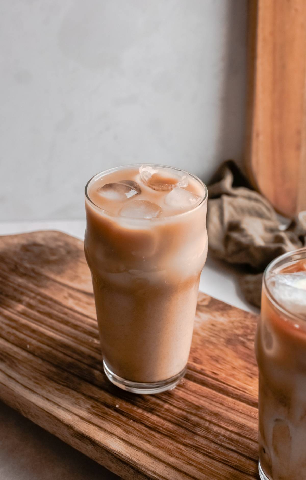 A glass of iced coffee with milk sits on a wooden board next to a brown cloth, styled like a Copycat Starbucks iced drink featuring homemade brown sugar syrup.