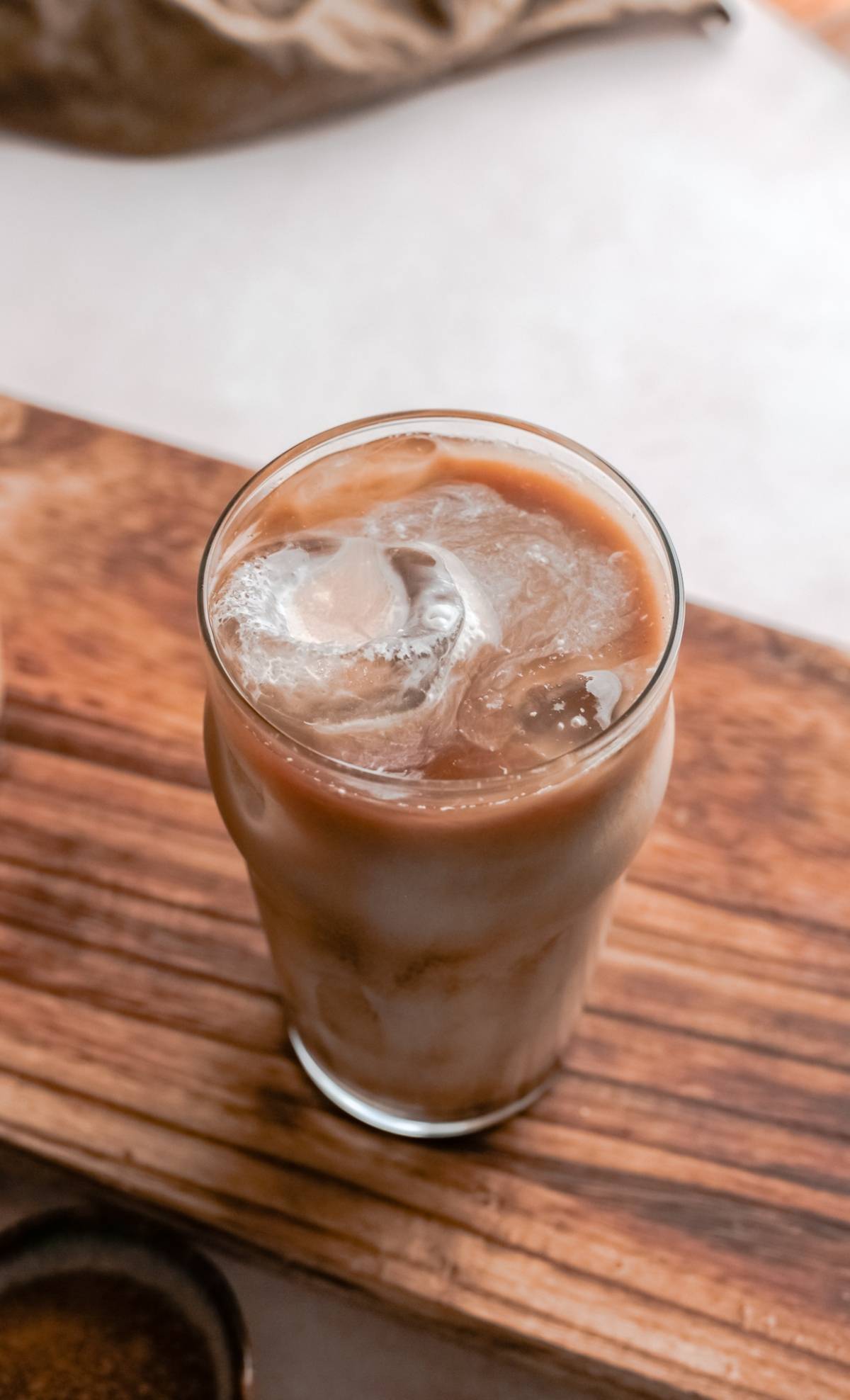 A glass of iced coffee with milk sits on a wooden surface, sweetened with homemade brown sugar syrup—perfect for making a Starbucks Copycat Iced Brown Sugar Oatmilk Shaken Espresso at home.