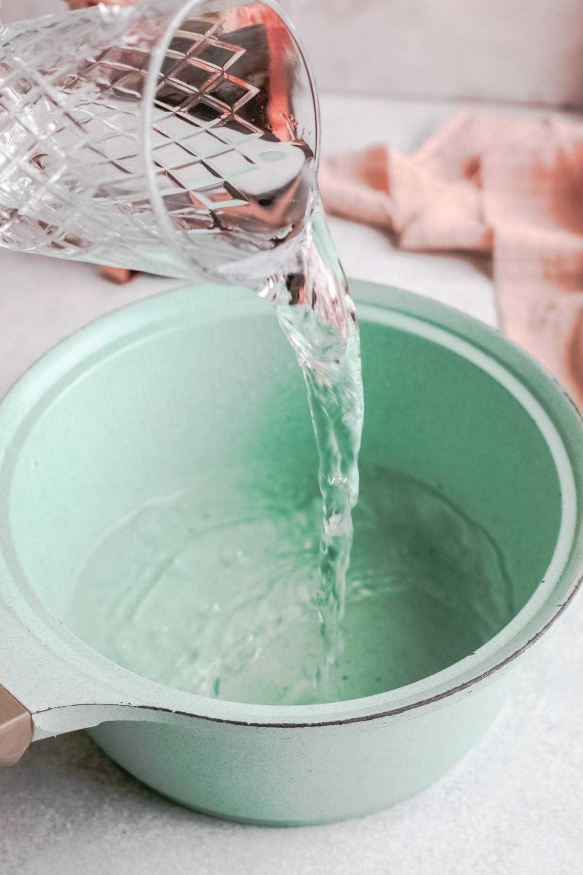 Water being poured from a glass into a light green saucepan on a kitchen counter—perfect prep for making a Starbucks Copycat Iced Brown Sugar Oatmilk Shaken Espresso at home.