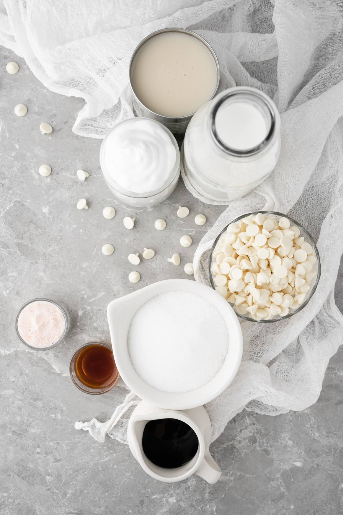 Top view of baking ingredients: white chocolate chips, sugar, milk, vanilla, whipped cream, salt, and chocolate syrup—everything you need for a delicious DIY white chocolate mocha iced coffee.
