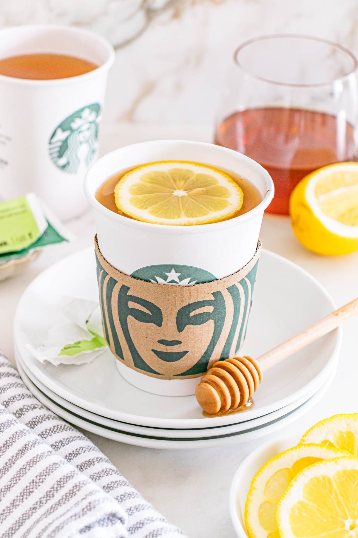 Starbucks tea with a lemon slice on top, honey dipper, and lemon slices on a white plate.