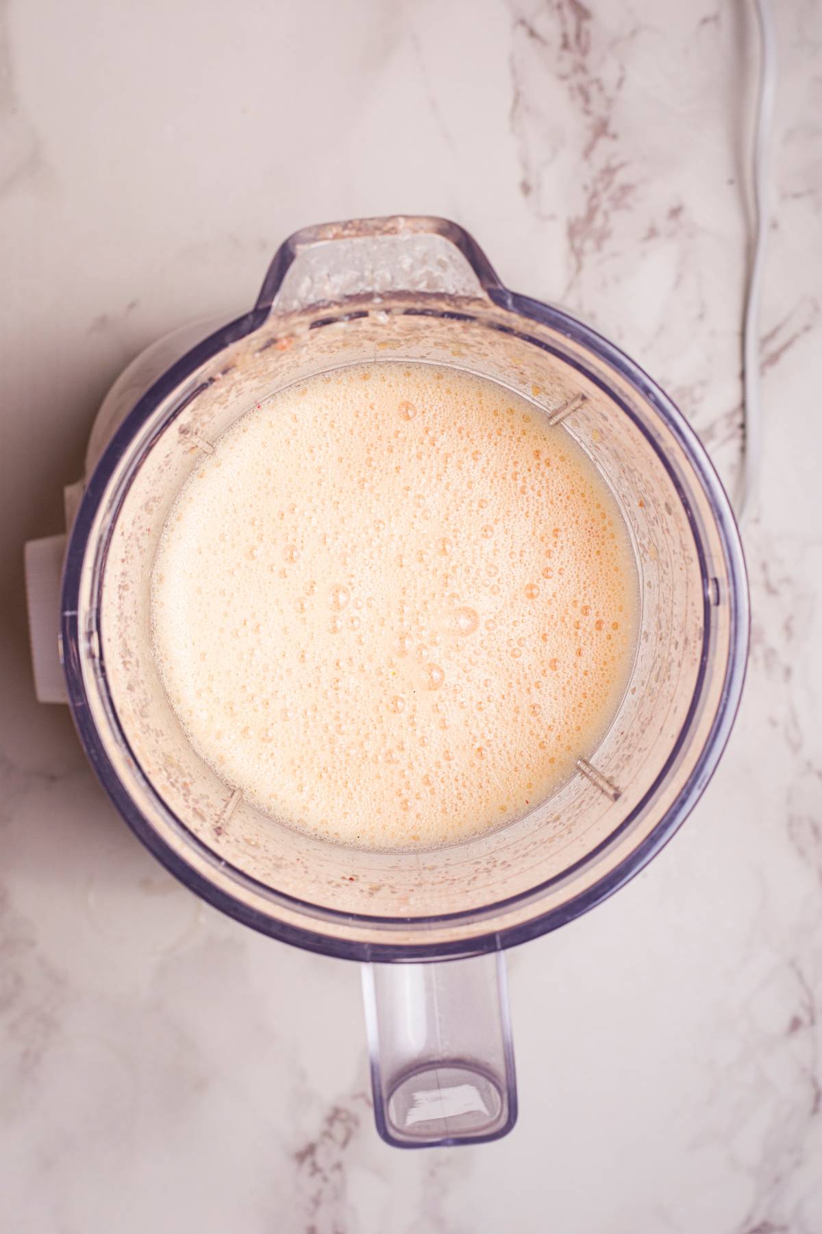 Top view of a blender filled with a frothy, light orange smoothie on a marble countertop—perfect for trying out your own DIY Starbucks lemonade recipe or refreshing summer Starbucks drink recipe.