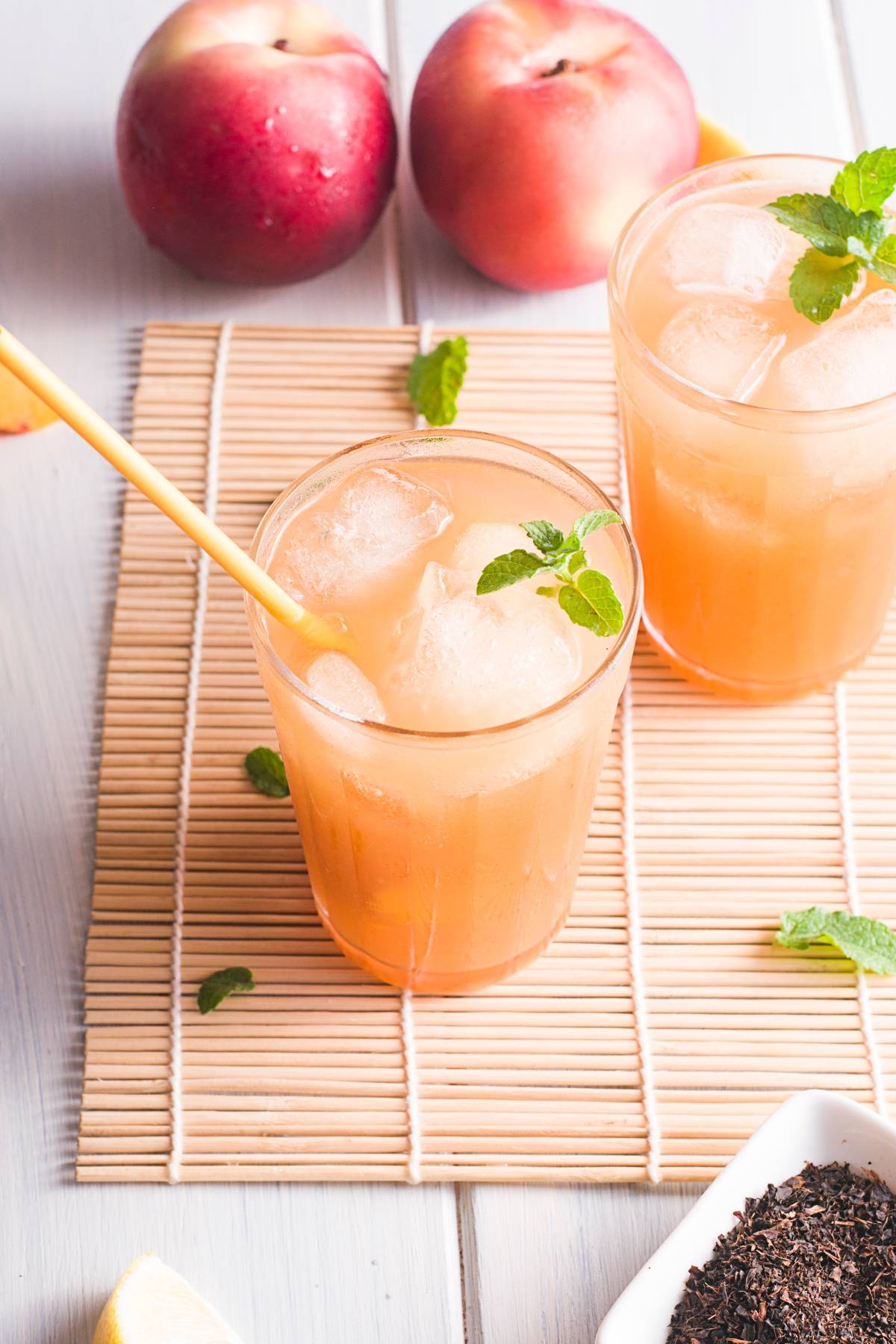 Iced peach tea with mint in glasses on a bamboo mat, fresh peaches and tea leaves in the background—perfect for a DIY Starbucks lemonade recipe or your own summer Starbucks drink recipe.
