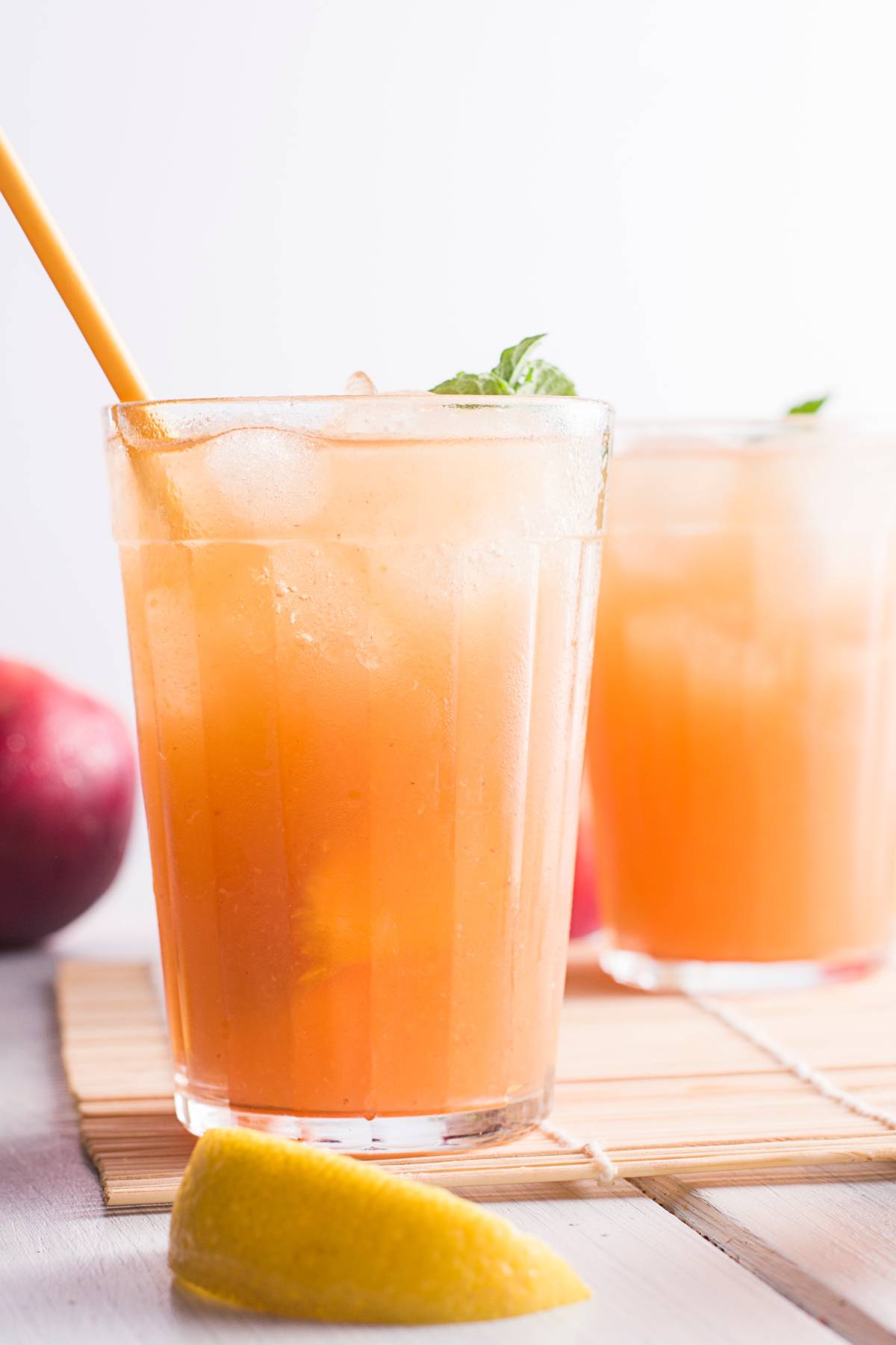 A glass of iced peach tea with a straw, garnished with mint, sits next to a lemon wedge and another drink—perfect for anyone craving a refreshing summer Starbucks drink recipe.