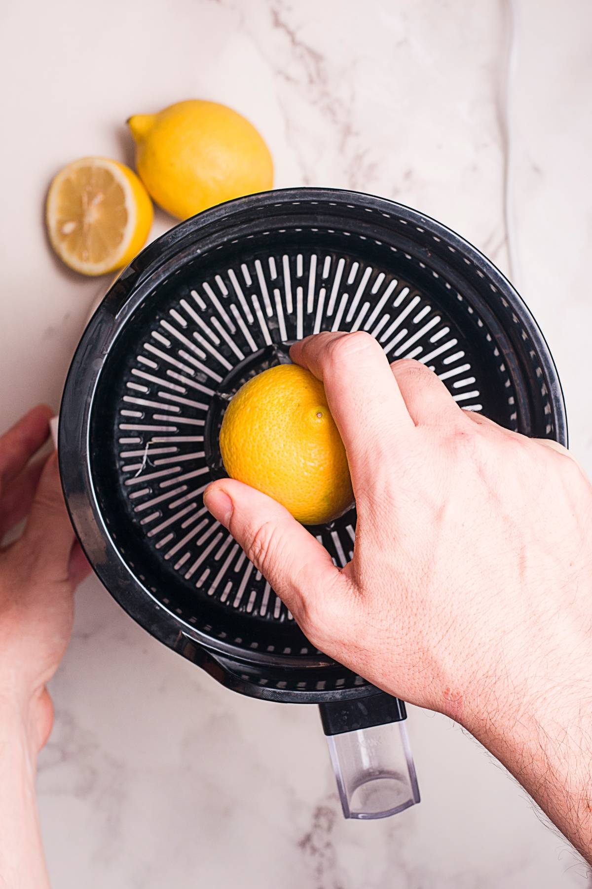 Hand pressing a lemon on a juicer, with two lemons on a marble countertop—perfect for making a refreshing Starbucks copycat peach black tea lemonade at home.