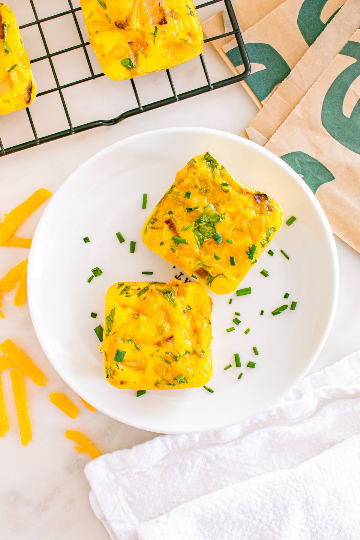 Two square egg bites with herbs on a white plate, garnished with chopped chives.