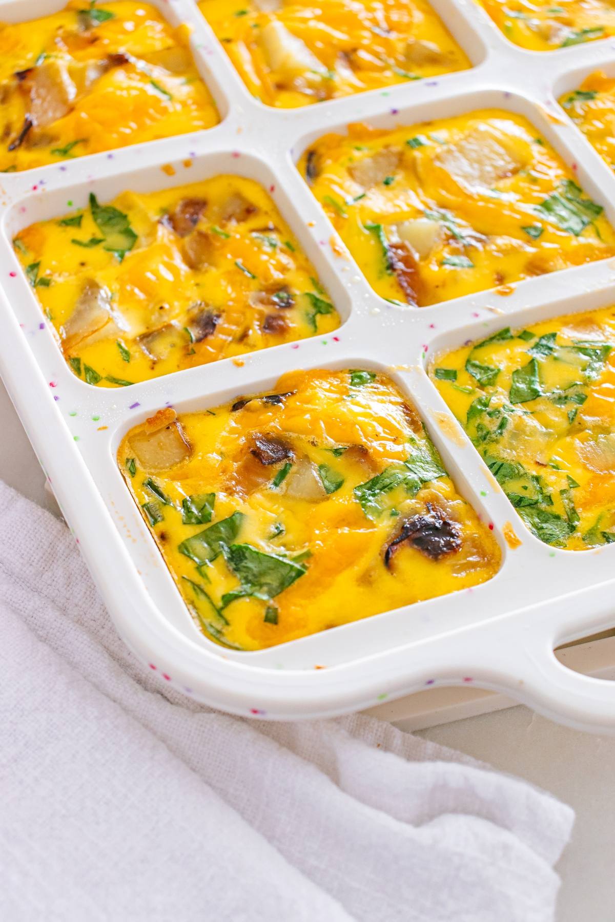 Mini egg bakes with spinach, cheese, and onions baked in a white silicone square mold on a countertop.