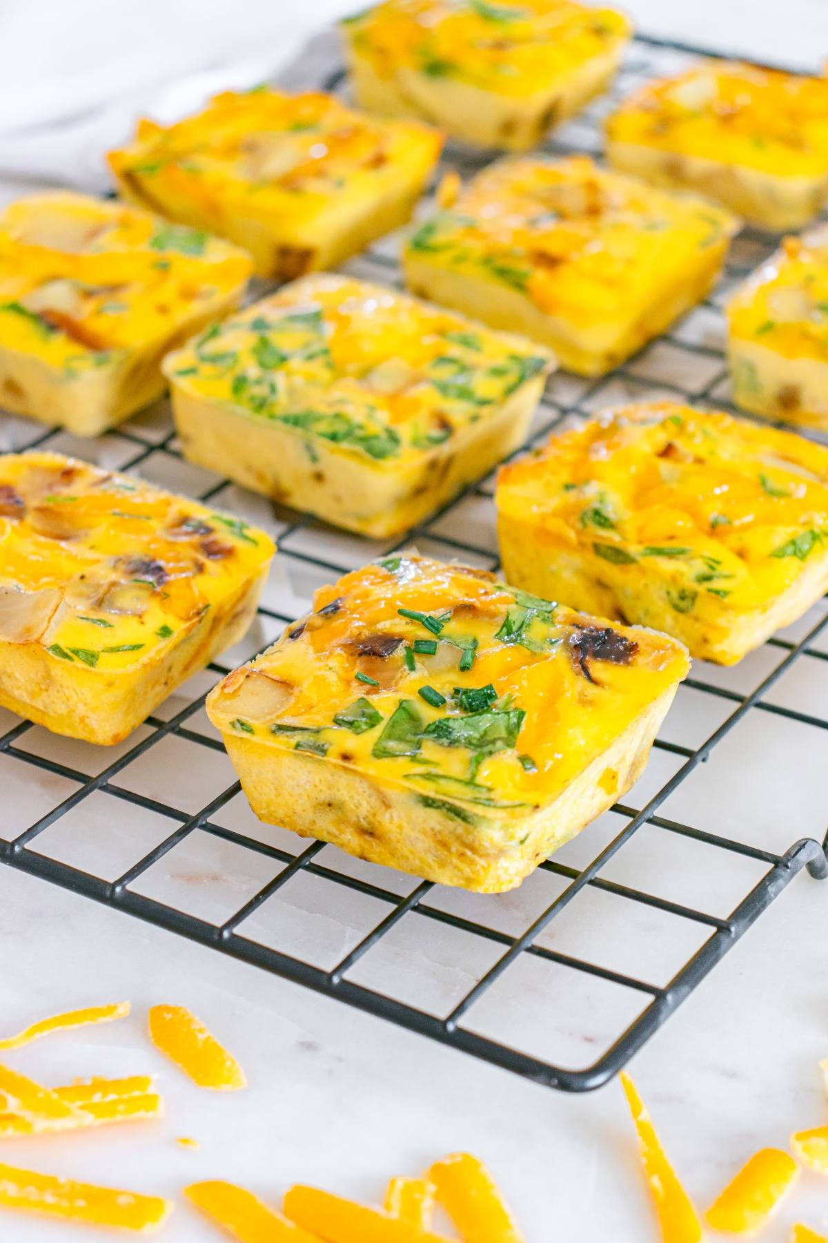 Square egg muffins with vegetables cooling on a wire rack, with shredded cheese scattered nearby.