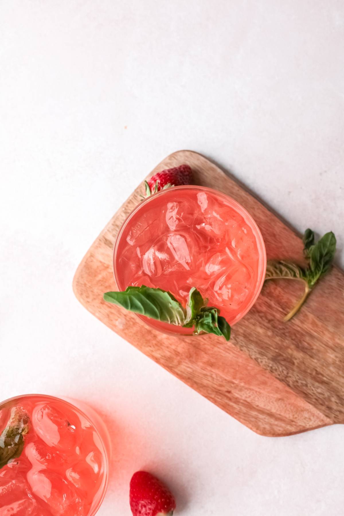 A pink iced cocktail with gin, garnished with basil and served on a wooden board, with fresh strawberries nearby.