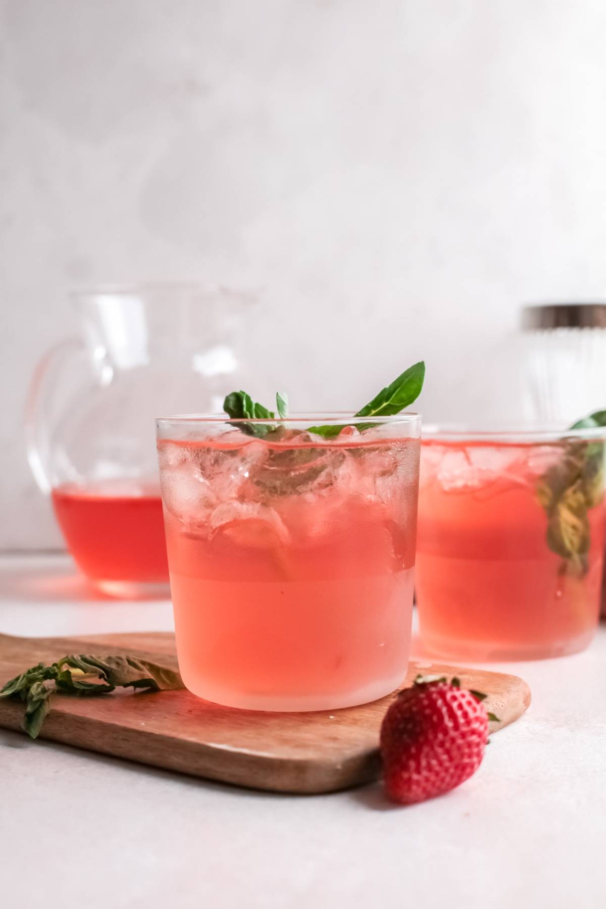 Two glasses of refreshing summer cocktail with mint leaves, a strawberry, and a pitcher in the background—perfect for enjoying a strawberry gin rickey on a warm day.