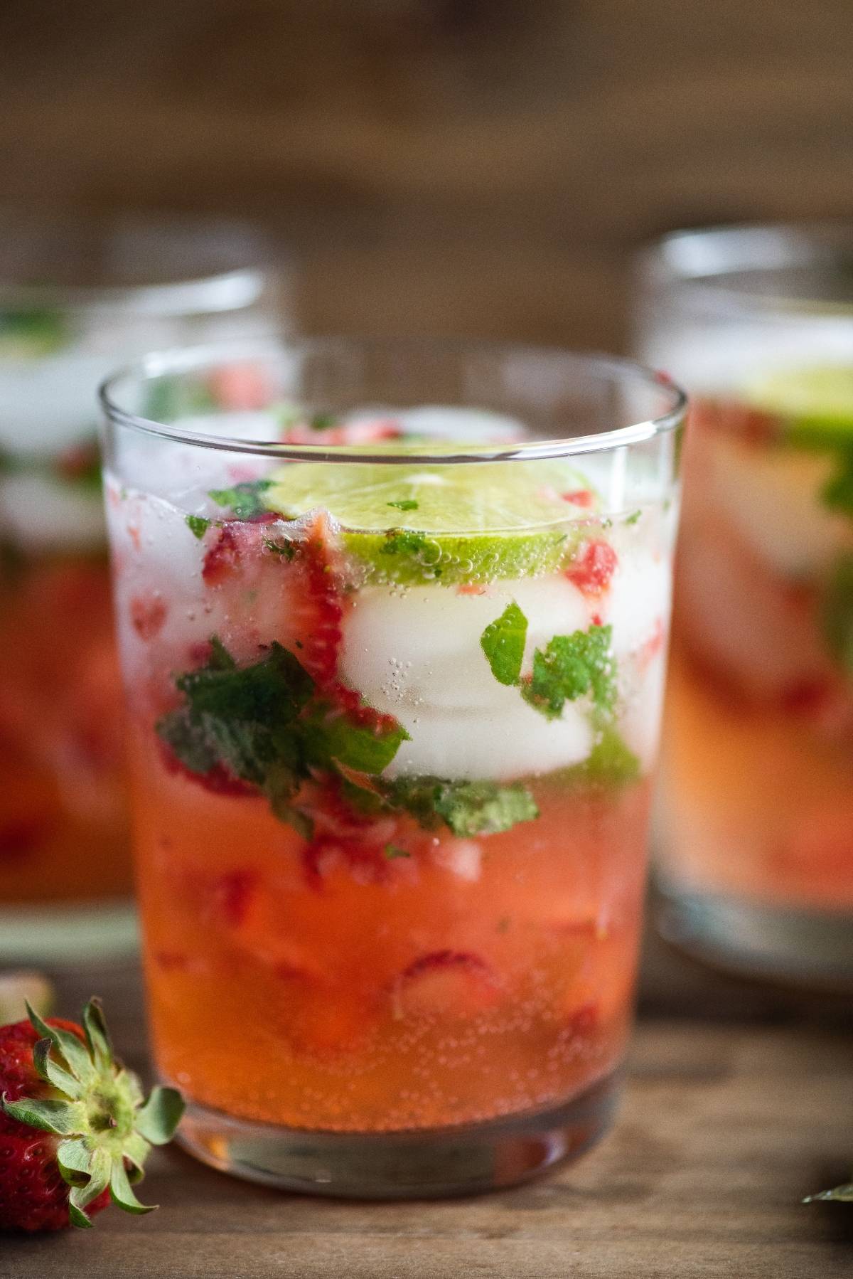 A glass of strawberry mojito with lime slices, mint leaves, and ice, garnished with fresh strawberries—a refreshing cocktail with white rum perfect for an easy summer cocktail recipe.