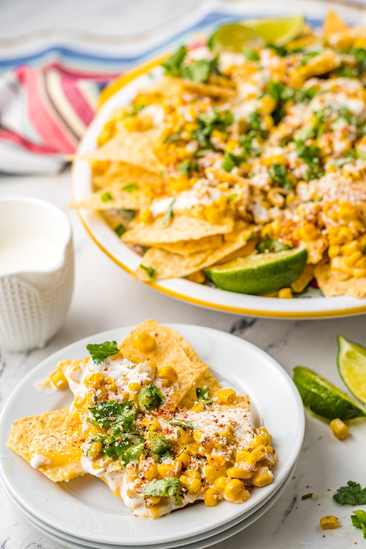 Plate of nachos topped with corn, cheese, cilantro, and sauce, with lime wedges on the side—a Mexican nachos recipe featuring unique nacho toppings for extra flavor.