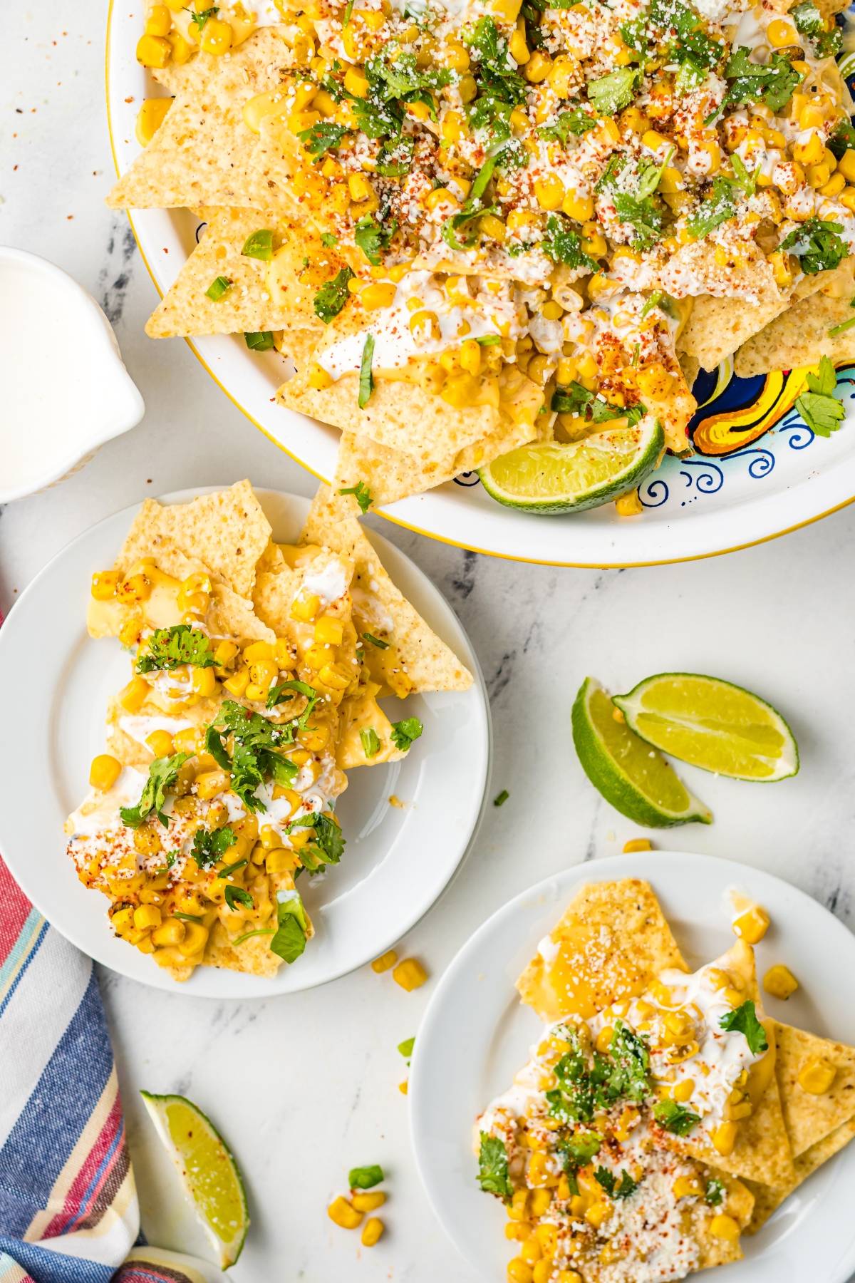 Tortilla chips topped with corn, cheese, sour cream, and herbs create delicious Street Corn Nachos, featuring unique nacho toppings and served with fresh lime wedges on the side.