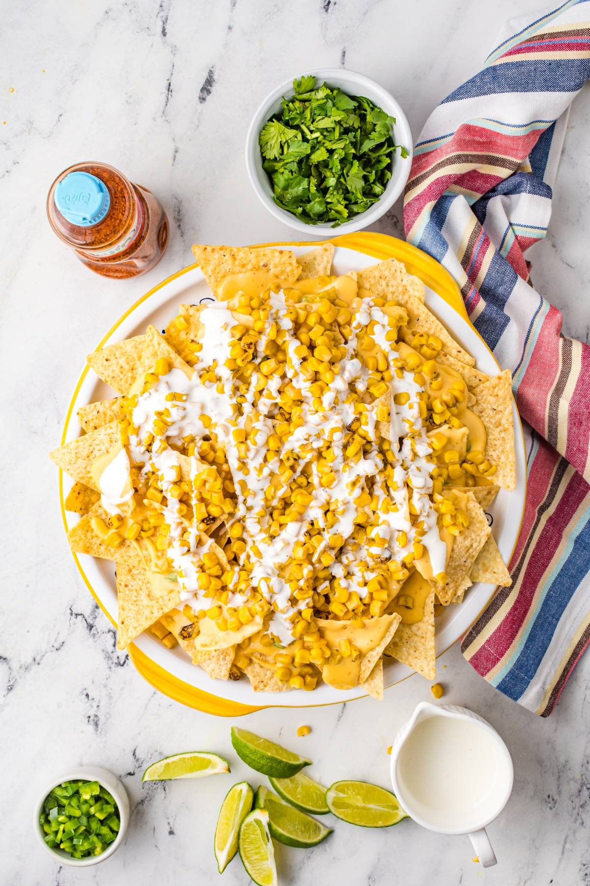 A plate of nachos with zesty cheese sauce, corn, and sour cream, served with lime wedges and extra toppings—the perfect Mexican nachos recipe.