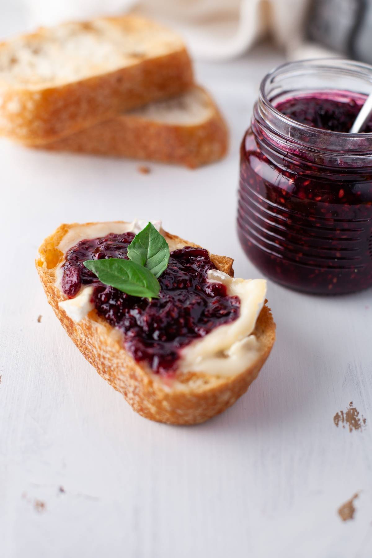 A slice of bread with butter and berry jam made with the easiest jam recipe, garnished with basil, next to a jar of fresh berry jam.