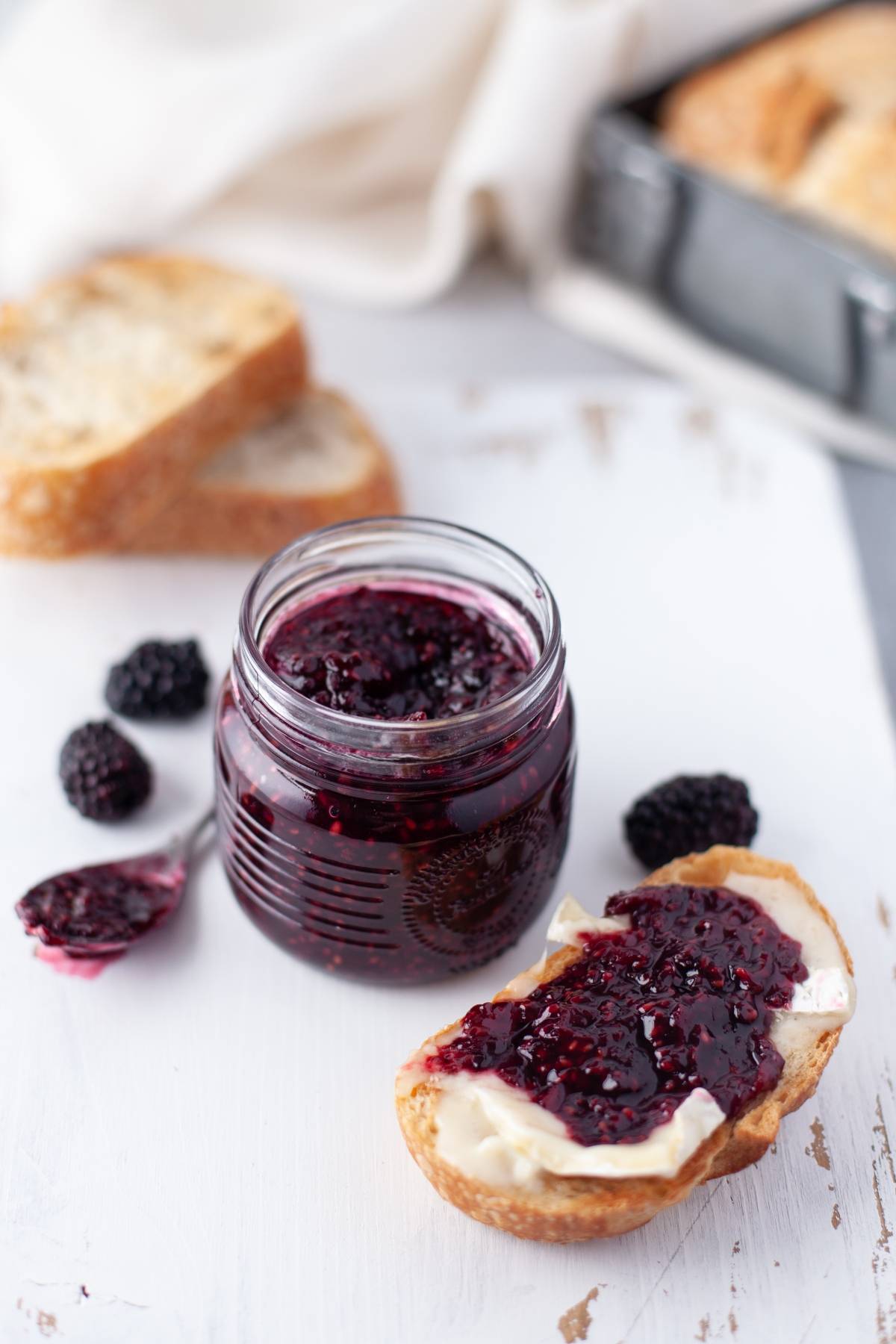 A jar of sugar free blackberry jam with a slice of bread spread with jam and butter, surrounded by fresh blackberries—perfect for those seeking a healthy homemade jam recipe.