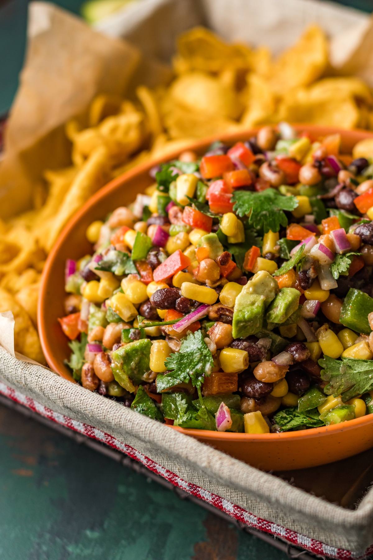 A bowl of colorful bean and corn salad with diced avocado, surrounded by tortilla chips—a vibrant Southwest vegan dip perfect as a healthy summer BBQ dip or colourful appetizer.