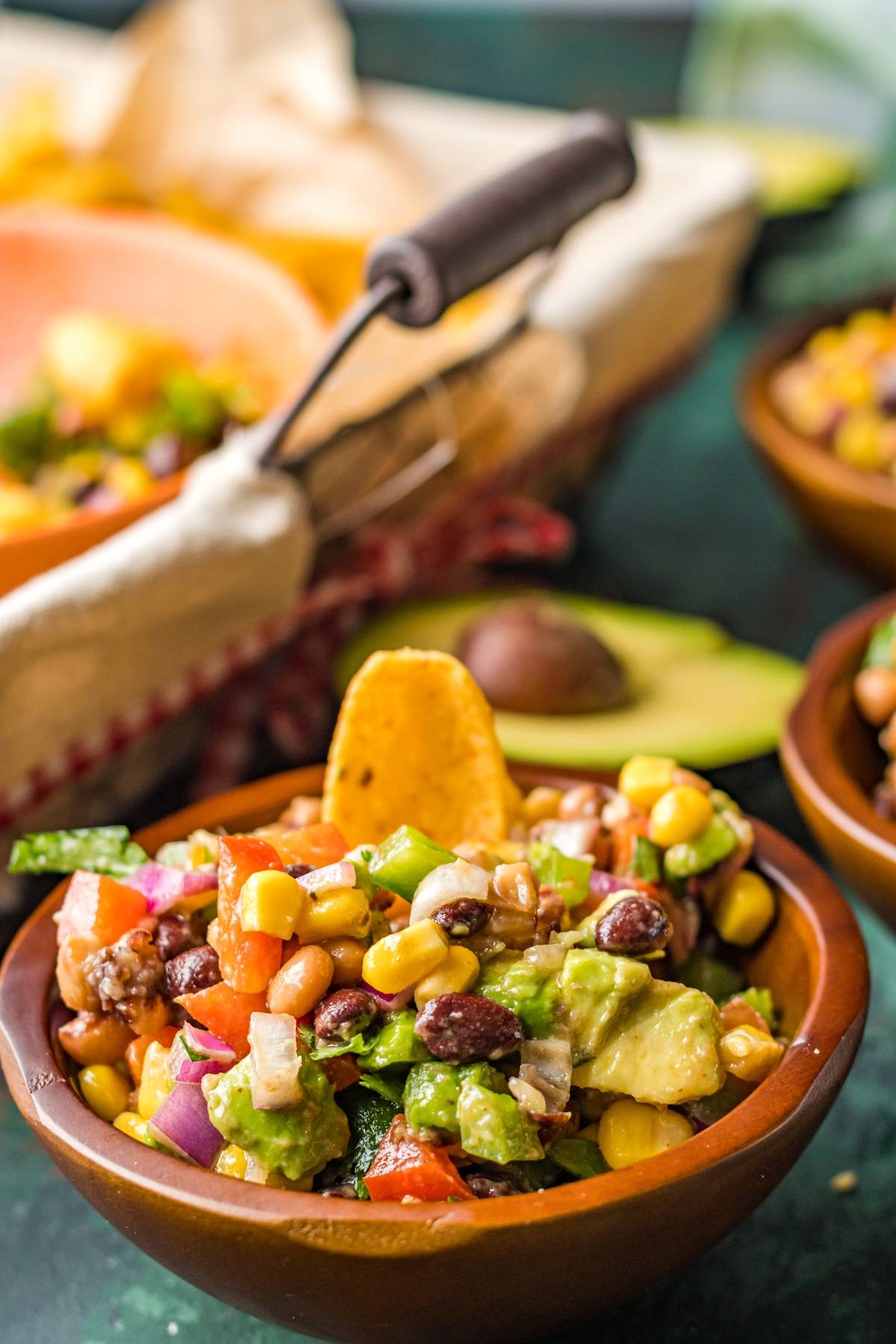 A wooden bowl of colorful cowboy caviar dip—a vibrant bean and corn salsa with avocado and a tortilla chip on top—makes for the perfect Southwest vegan dip.