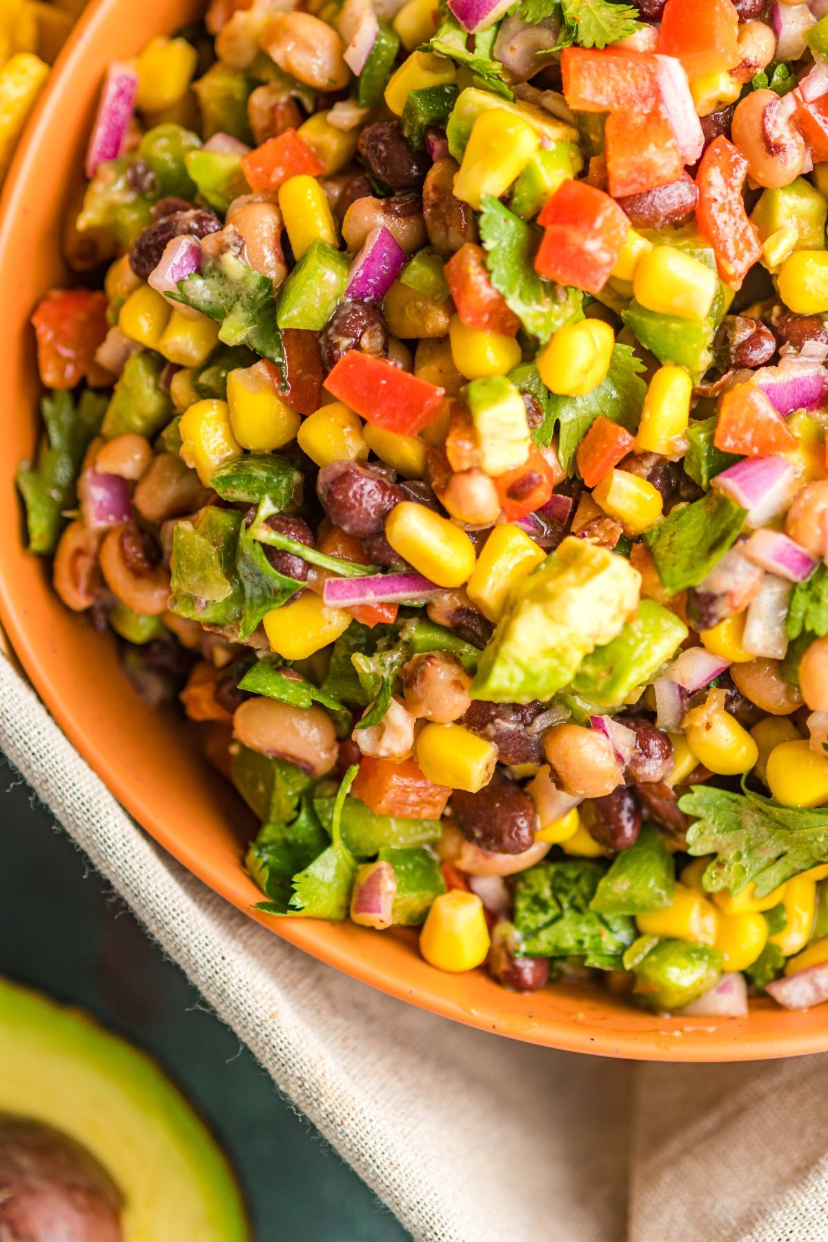 Colourful bean salad with corn, avocado, red onion, tomato, and cilantro in an orange bowl—a perfect Southwest vegan dip or vibrant bean and corn salsa for any colourful appetizer spread.
