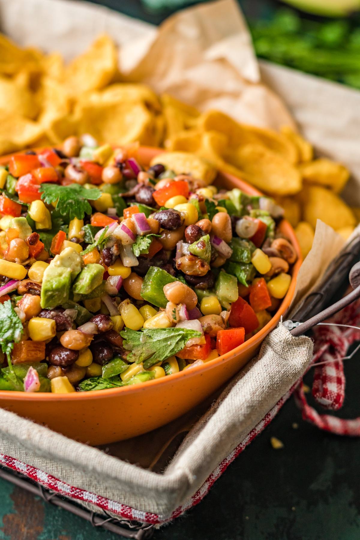 A bowl of Texas Cowboy Caviar dip—a colourful appetizer made with beans and corn—served with chips on the side in a rustic basket.